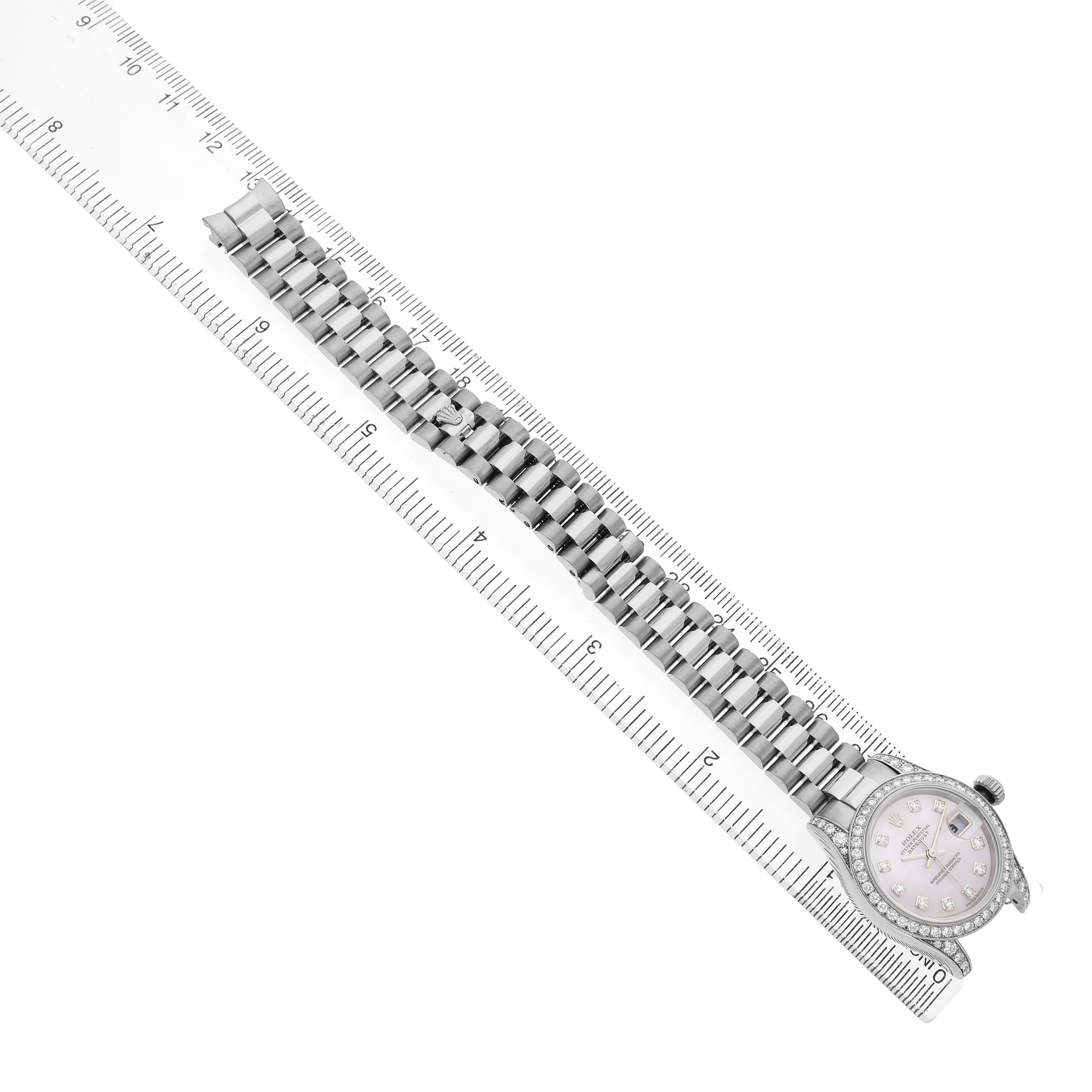 The Rolex President 179159 Women's White Gold Mother of Pearl Dial model watch is shown from a top-down angle, displaying the face and full bracelet alongside a ruler.