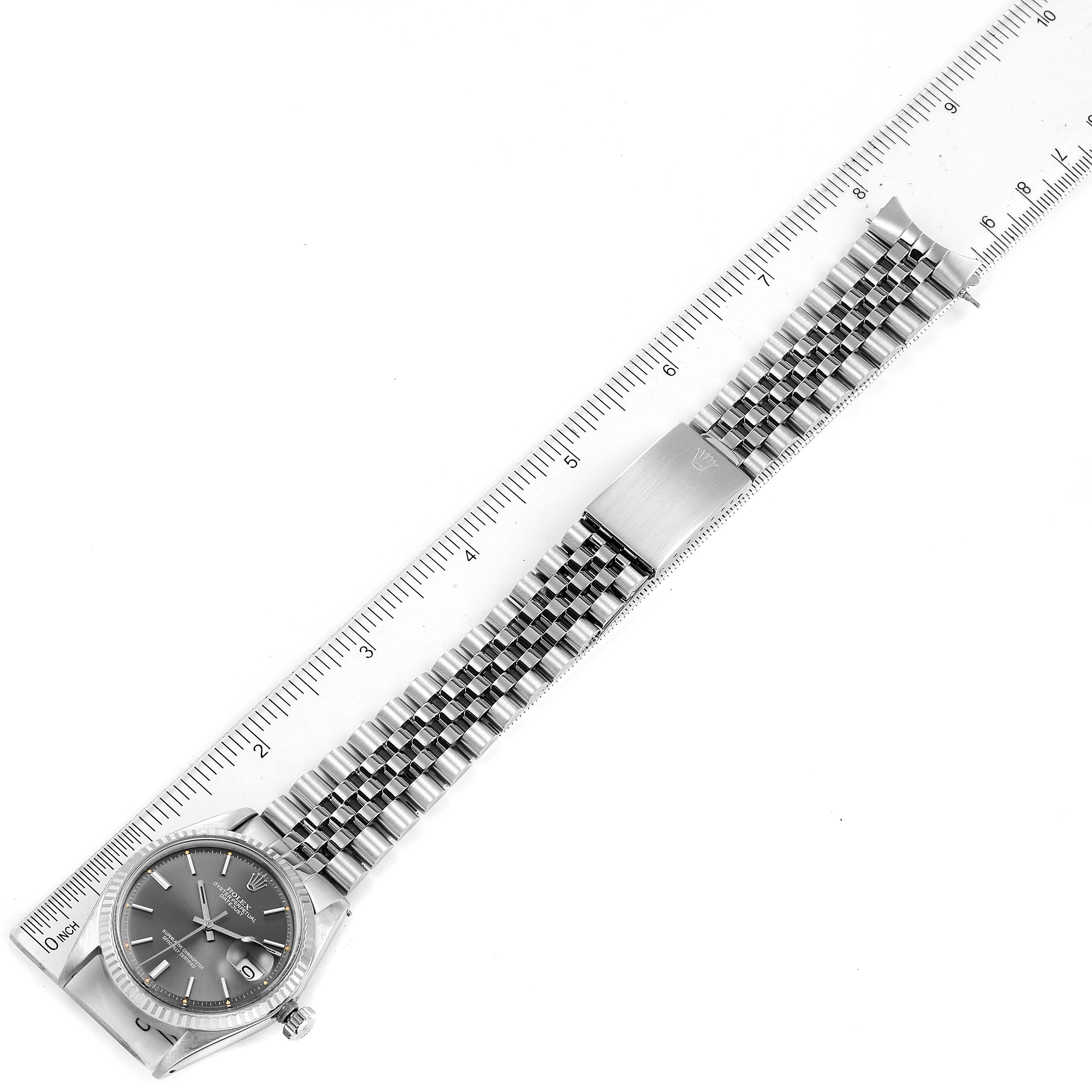 The image shows a Rolex Vintage Collection 1601 Men's Stainless Steel Grey Dial 1601 Men's Stainless Steel Grey Dial watch horizontally aligned next to a ruler, displaying its face, bracelet, and clasp.