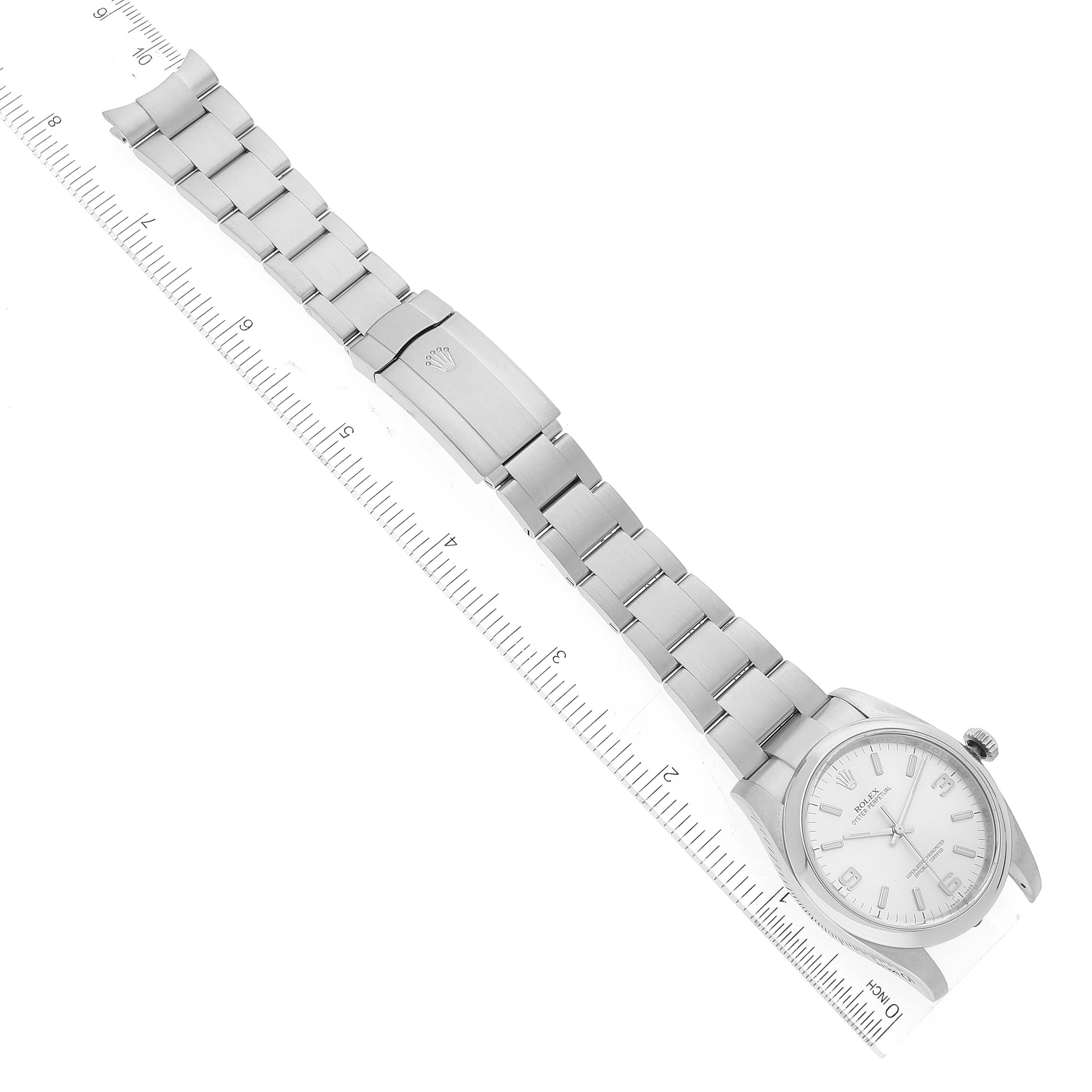 The image shows a side view of the Rolex Oyster Perpetual 116000 Men's Stainless Steel Silver Dial 116000 Men's Stainless Steel Silver Dial watch, displaying the face, bracelet, and clasp alongside a ruler for scale.