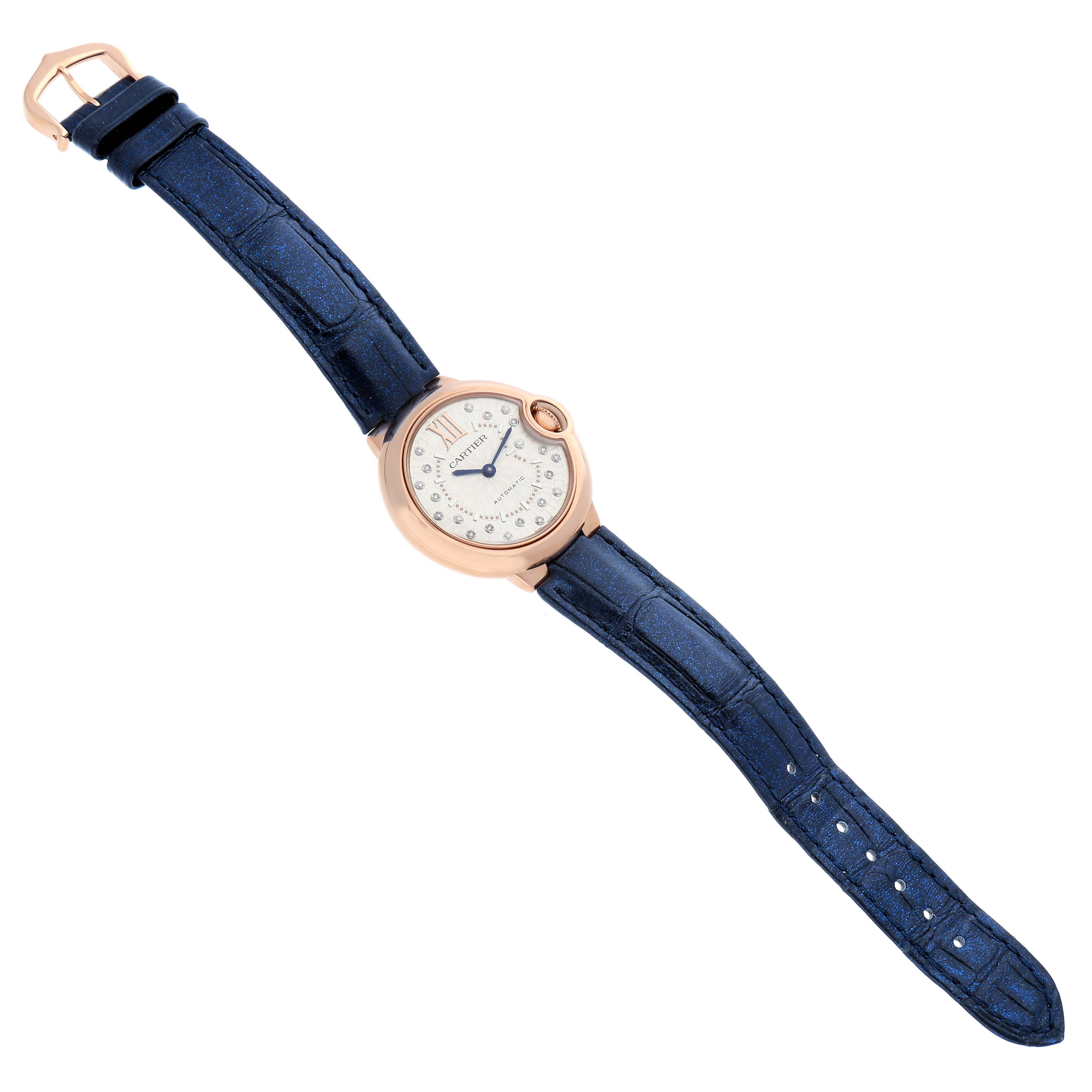 The Cartier Ballon Bleu WGBB0052 Women's Rose Gold Silver Dial watch is shown from a top view, featuring a round face, blue strap, and rose gold case.