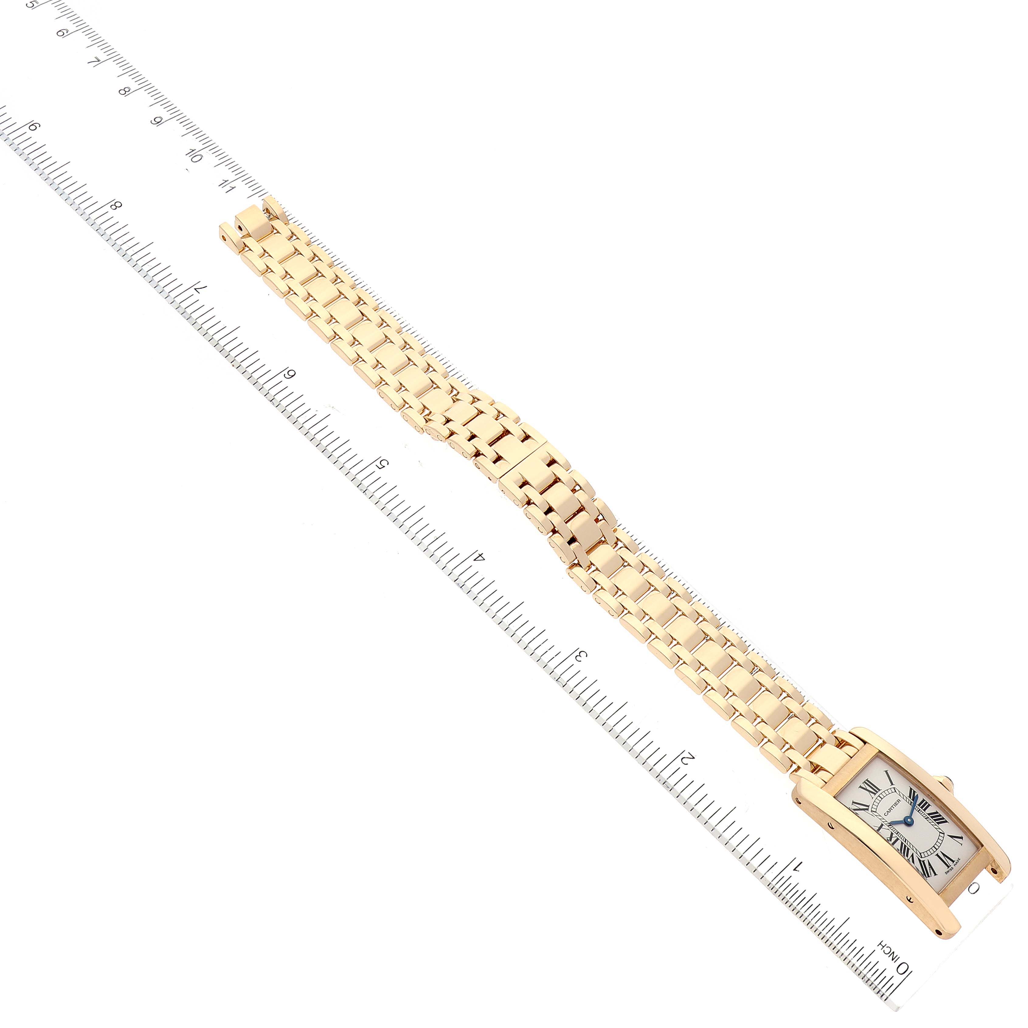 This image shows a Cartier Tank Américaine watch laid flat next to a ruler displaying the entire bracelet and face.