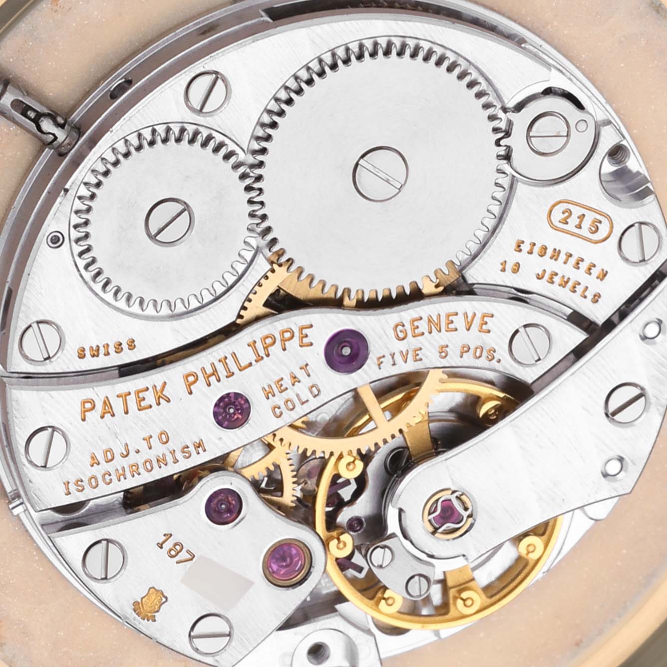 The image shows a close-up of the movement mechanism of the Patek Philippe Calatrava 3919J Men's Yellow Gold White Dial 3919J Men's Yellow Gold White Dial watch, highlighting gears and inscriptions.