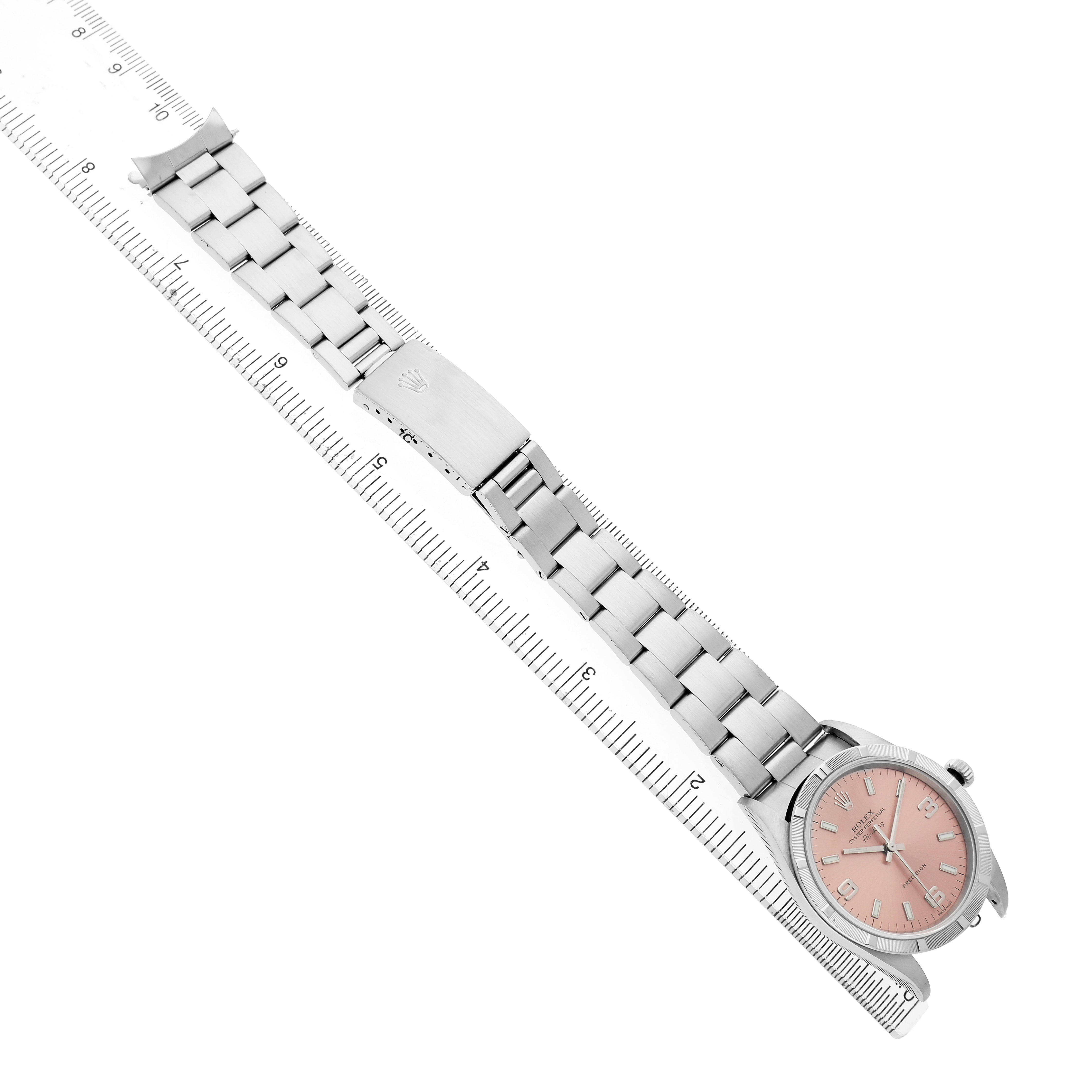 The Rolex Air-King 14010 Men's Stainless Steel Pink Dial watch is shown from a top angle, displaying the bracelet, clasp, and face against a ruler background.