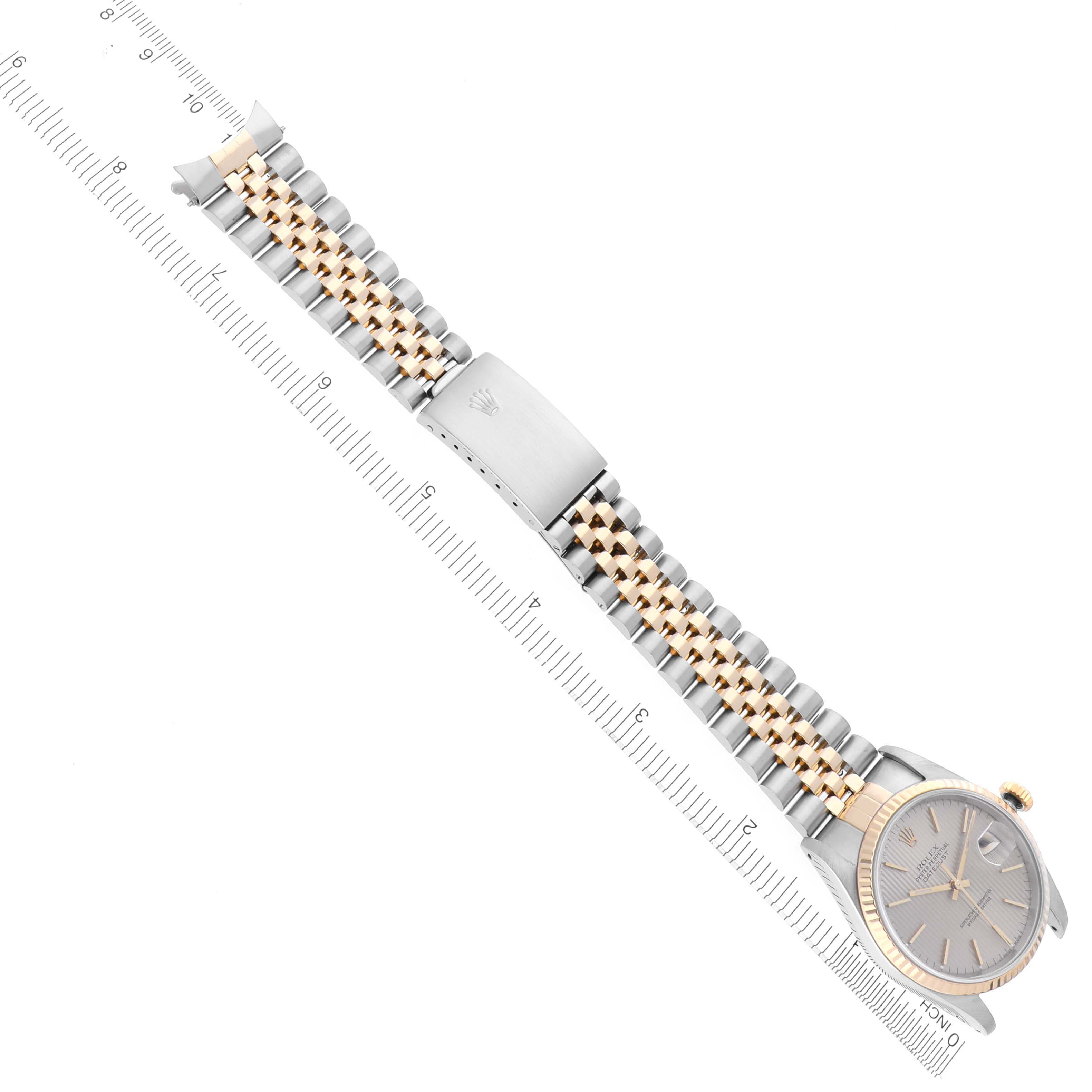 The Rolex Datejust 16233 Men
s Steel and Gold (two tone) Silver Dial 16233 Men
s Steel and Gold (two tone) Silver Dial watch is shown from a top-down angle, displaying the face, bezel, and jubilee bracelet alongside a ruler.