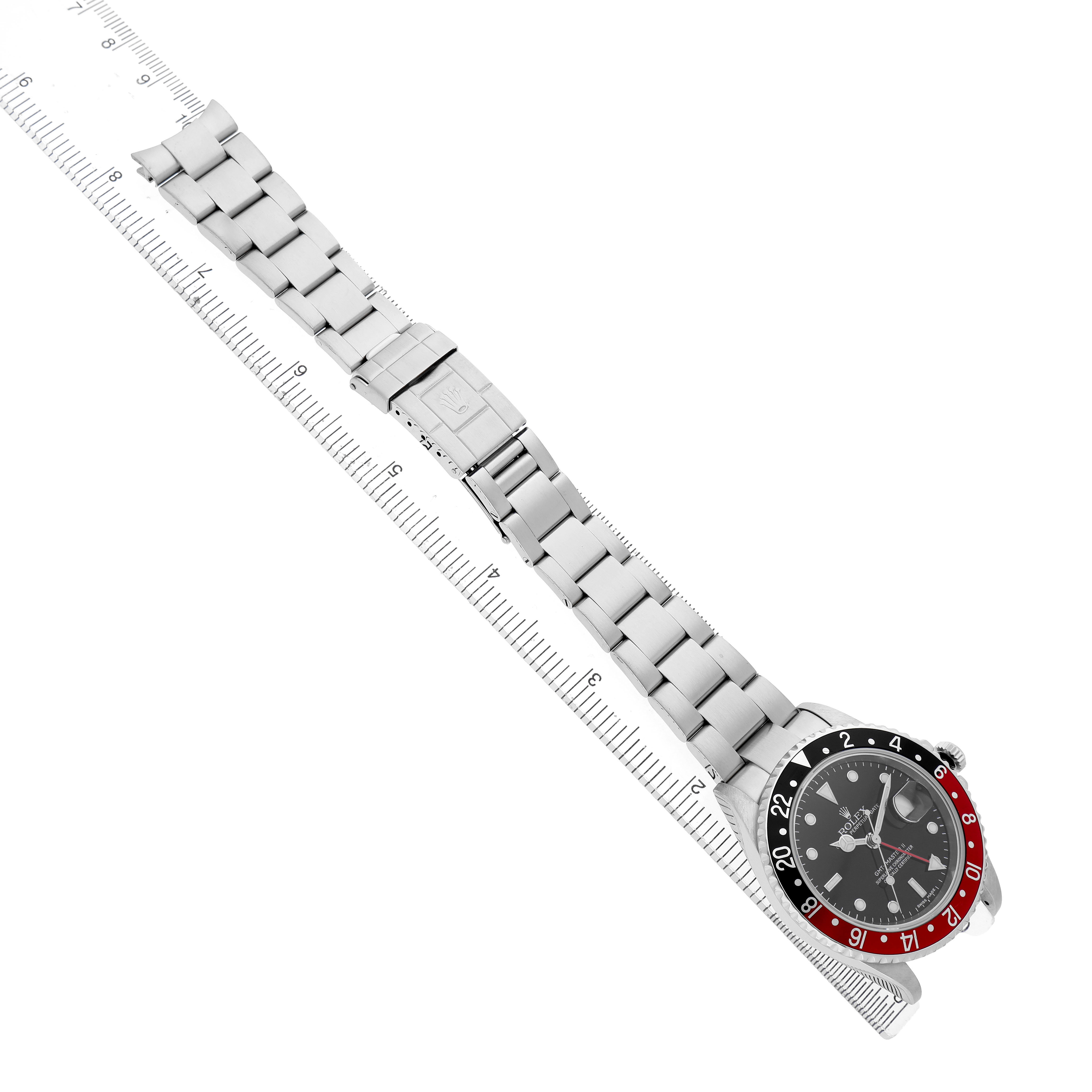 The Rolex GMT-Master 16710 Men's Stainless Steel Black Dial watch is shown at an angled top-down view, highlighting the face, bezel, and metal bracelet, with a ruler for scale.