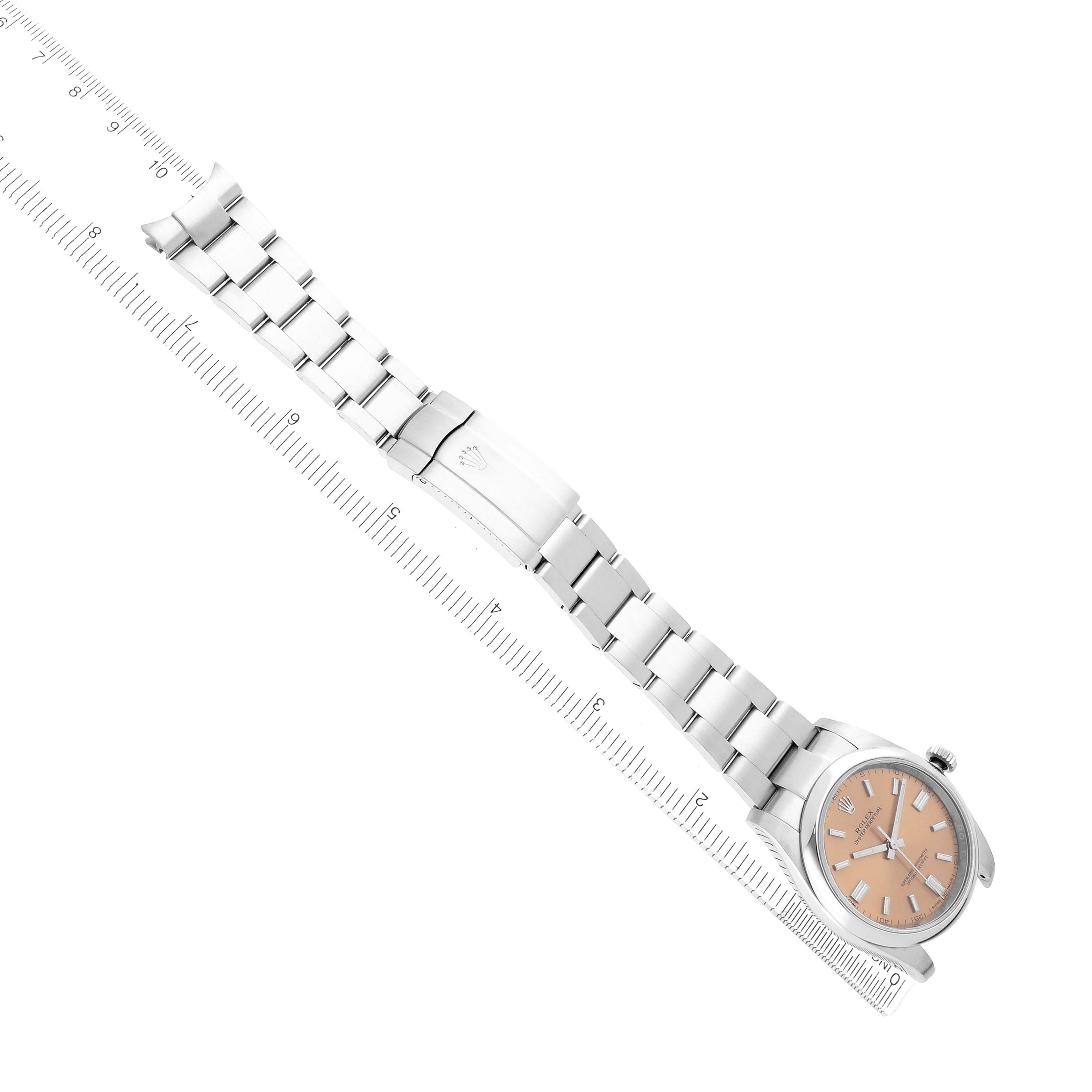 The Rolex Oyster Perpetual 116000 Men
s Stainless Steel Champagne Dial watch is shown from an overhead angle, highlighting the face, bracelet, and clasp alongside a ruler.