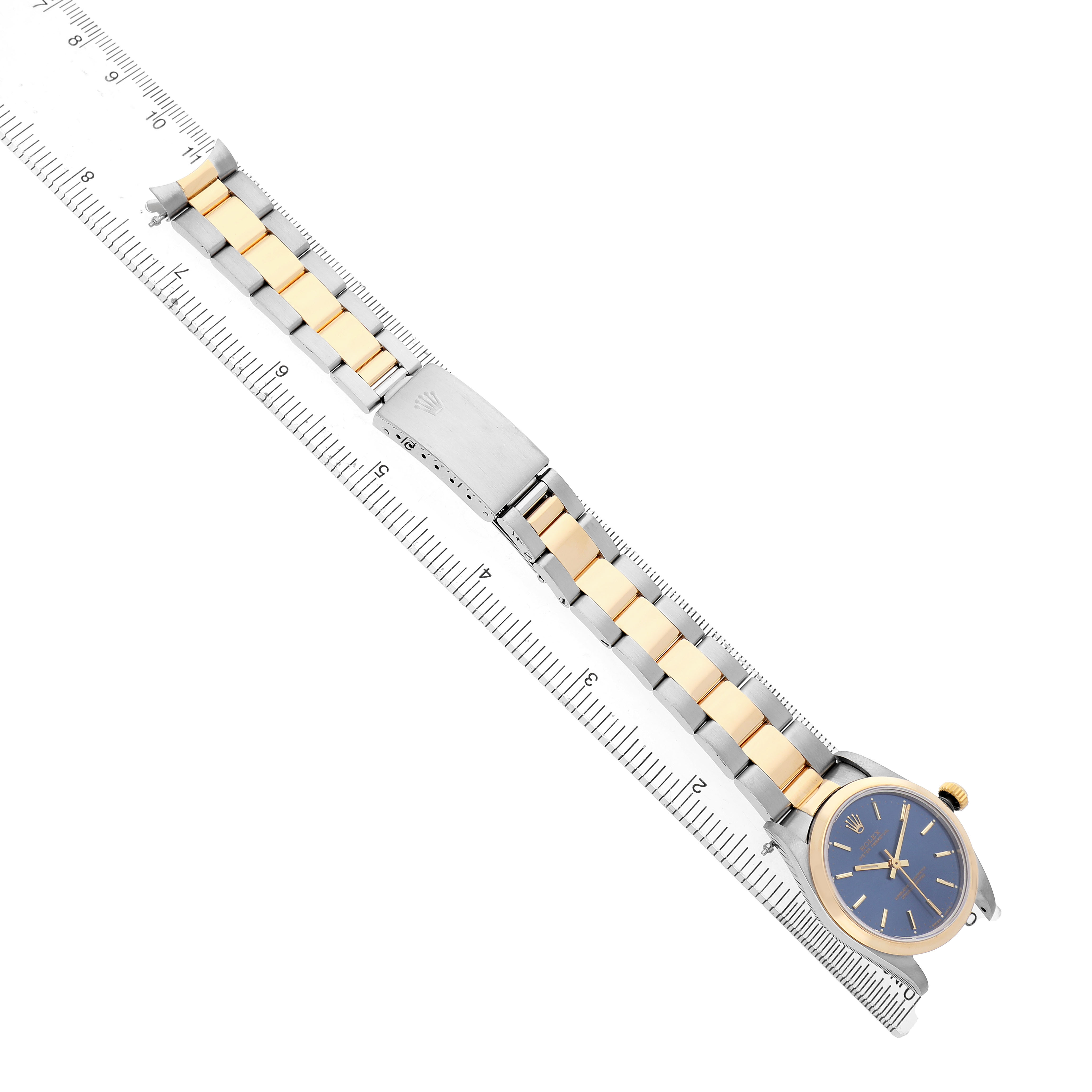 The Rolex Oyster Perpetual 67483 Women's Steel and Gold (two tone) Blue Dial watch is shown from a top view, highlighting its bracelet and clasp against a ruler.
