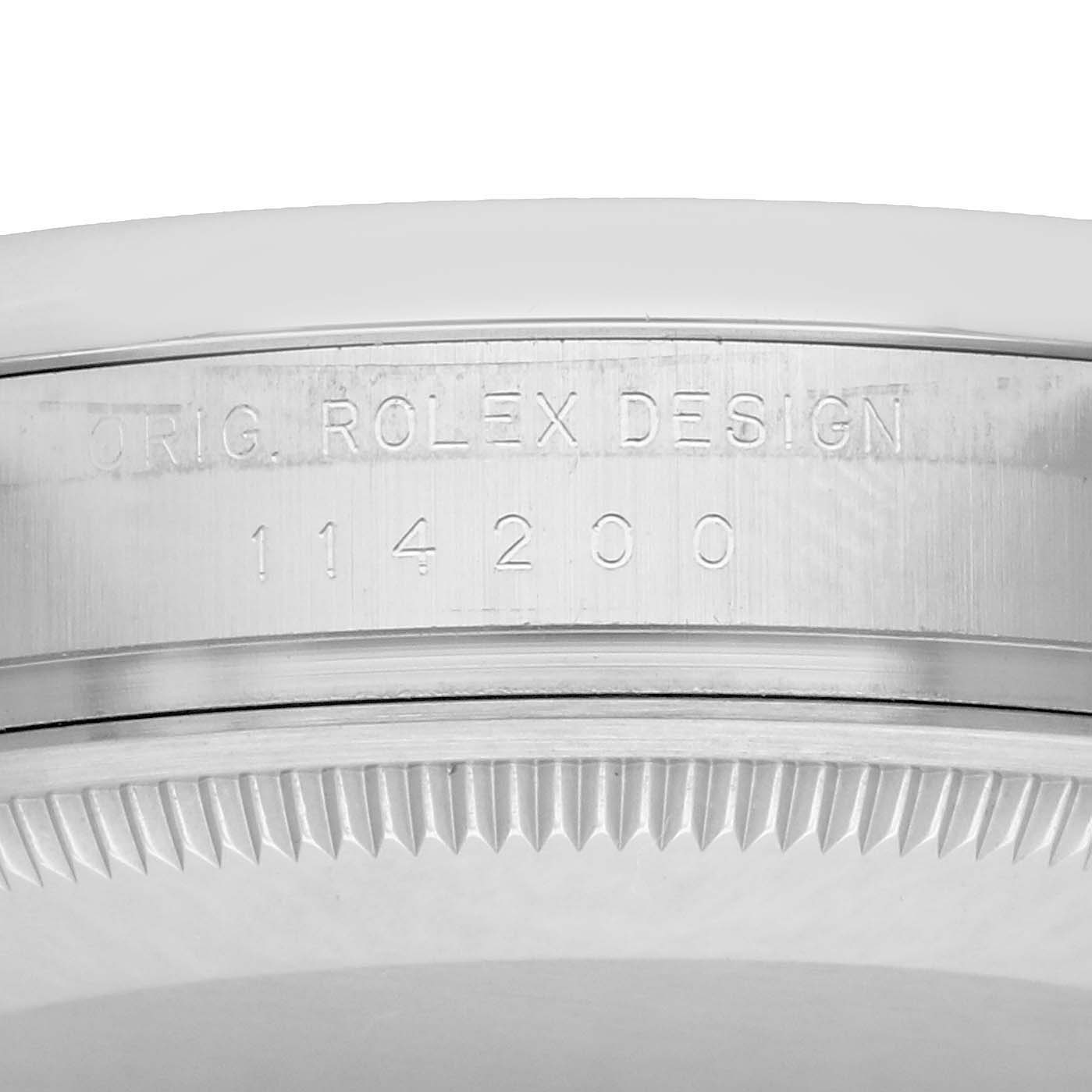The image shows the side view of the case and bezel of a Rolex Oyster Perpetual 114200 Men's Stainless Steel Green Dial, displaying the engraving "ORIG. ROLEX DESIGN 114200".
