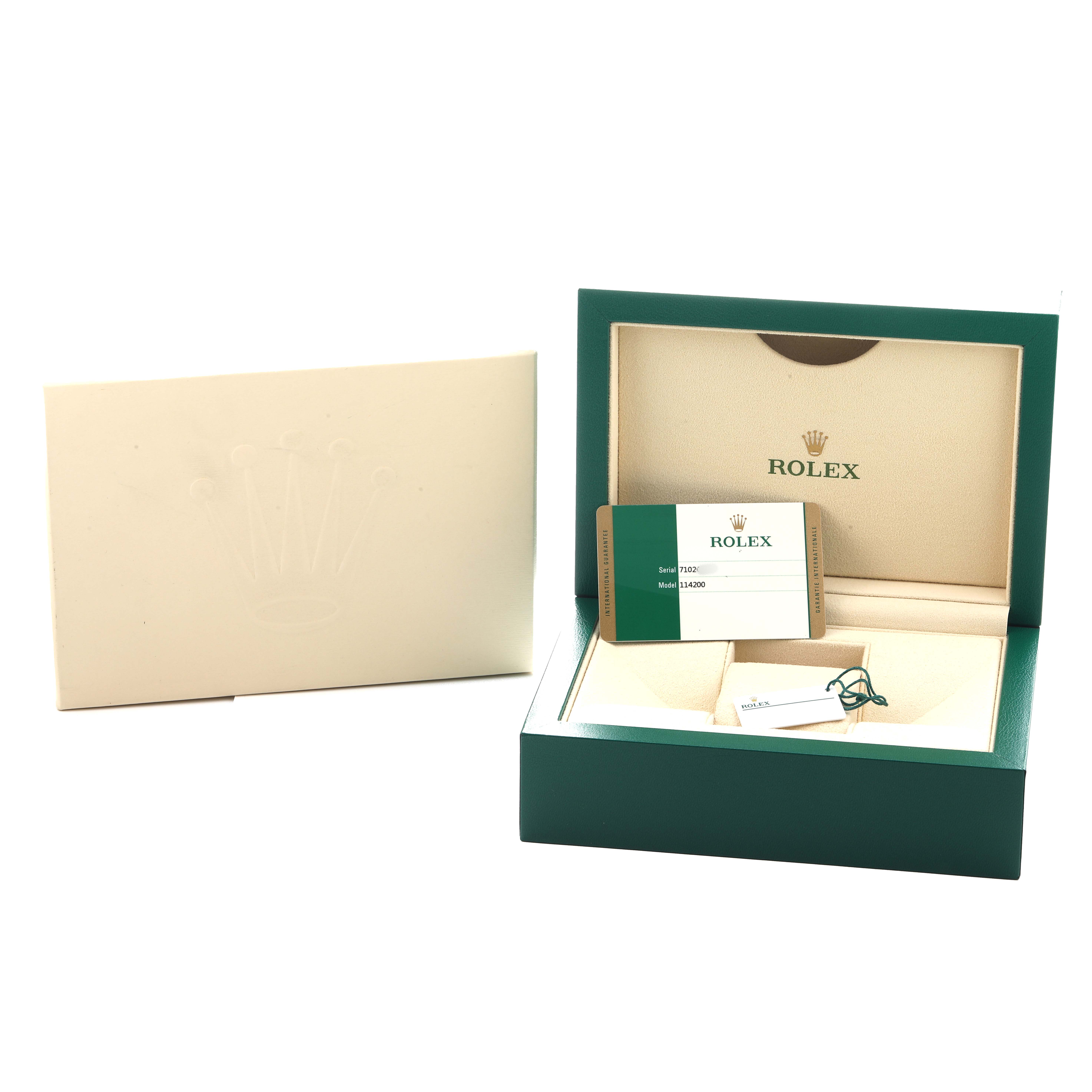 The image shows the packaging and accessories for a Rolex Oyster Perpetual 114200 Men's Stainless Steel Green Dial, including a box, warranty card, and tag.