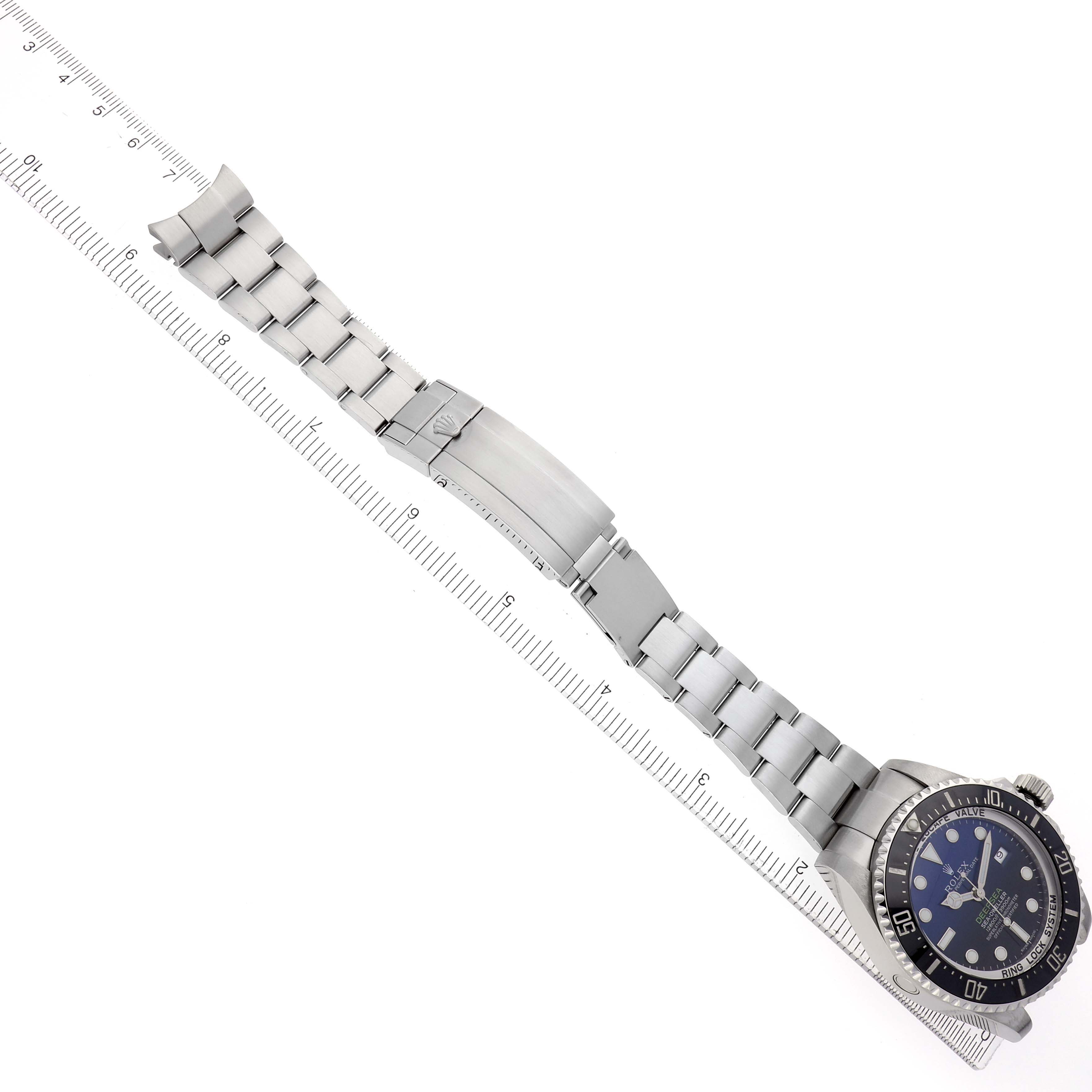 The Rolex Sea-Dweller 116660 Men's Stainless Steel Blue Dial watch is shown from an overhead angle, featuring its bracelet, clasp, and watch face alongside a ruler.