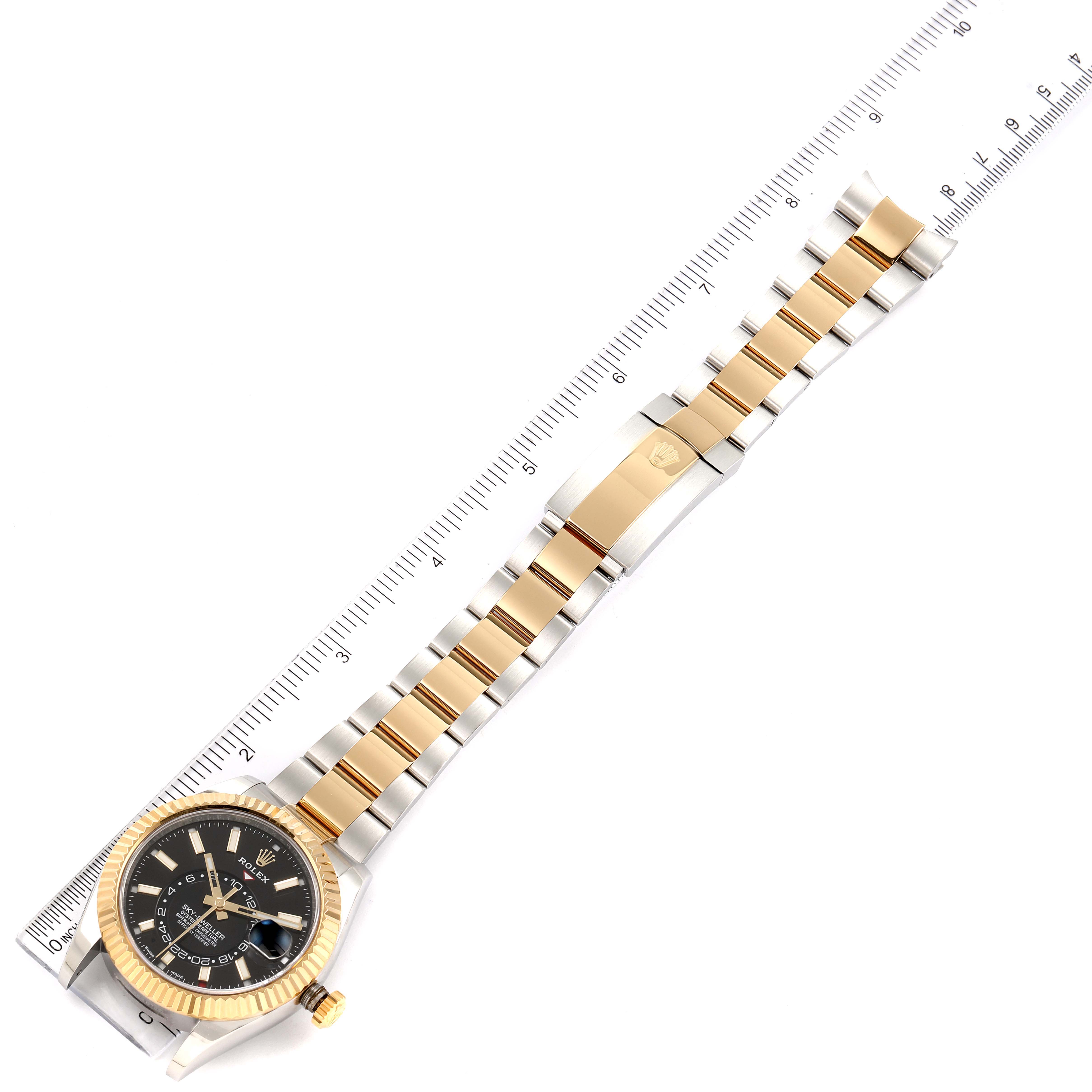 The image shows a Rolex Sky-Dweller 326933 Men's Steel and Gold (two tone) Black Dial 326933 Men's Steel and Gold (two tone) Black Dial watch, focusing on its full bracelet, clasp, and face, laid alongside a ruler.