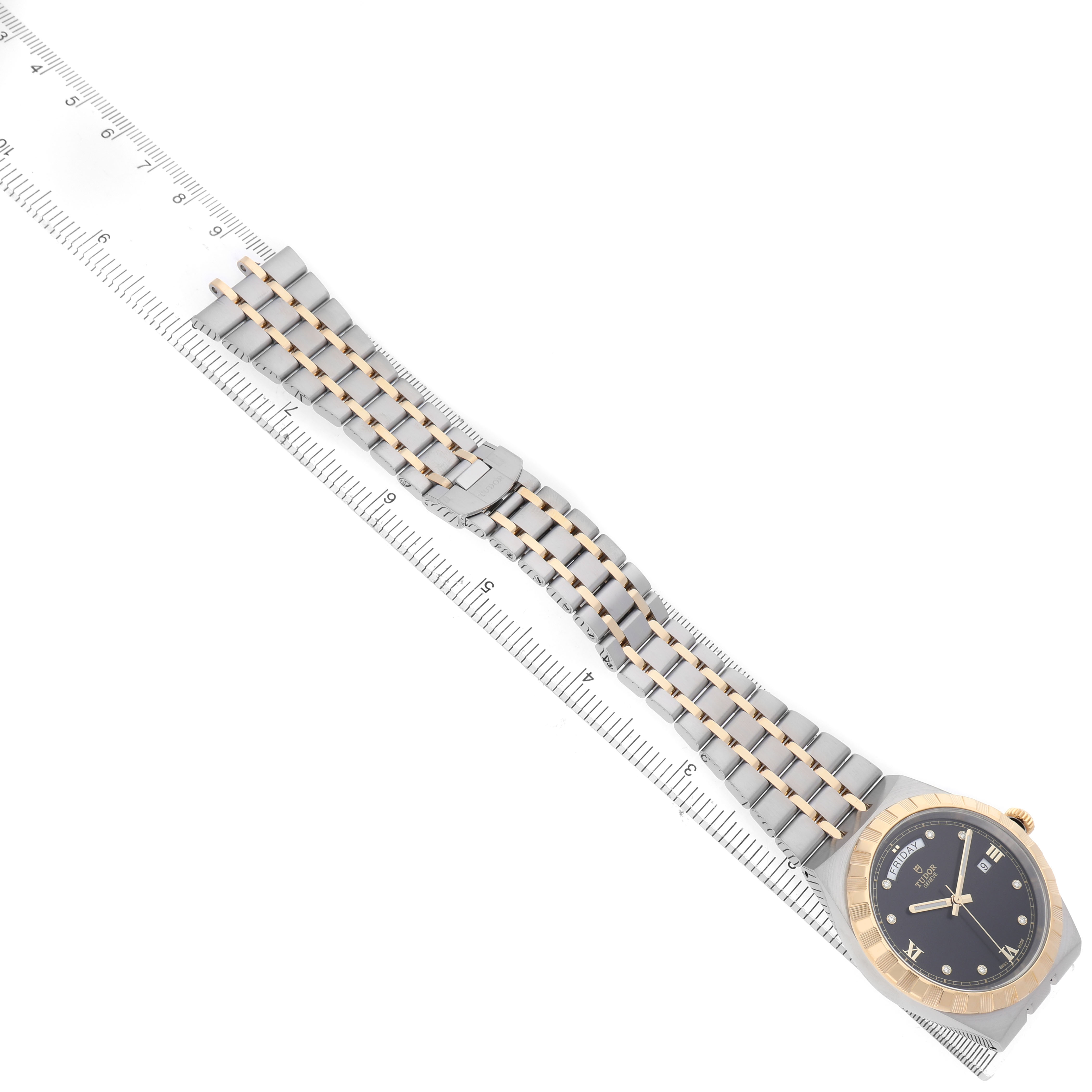 The Tudor Royal 28603 Men's Stainless Steel Black Dial watch is shown from a top-down angle with its face and full bracelet visible next to a ruler.