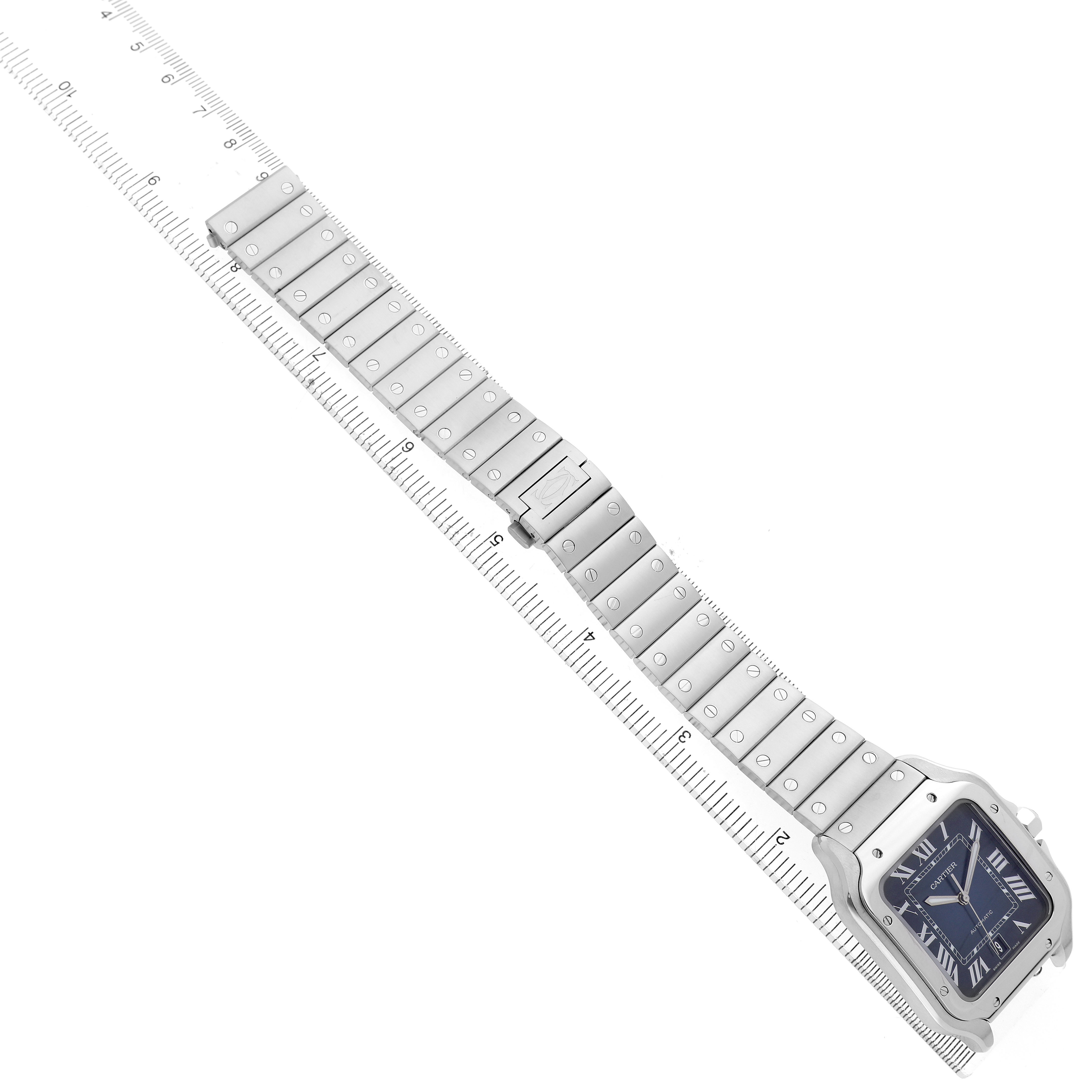The Cartier Santos WSSA0030 Men's Stainless Steel Black Dial watch is shown from a top angle, displaying its face and full metal bracelet alongside a ruler for scale.