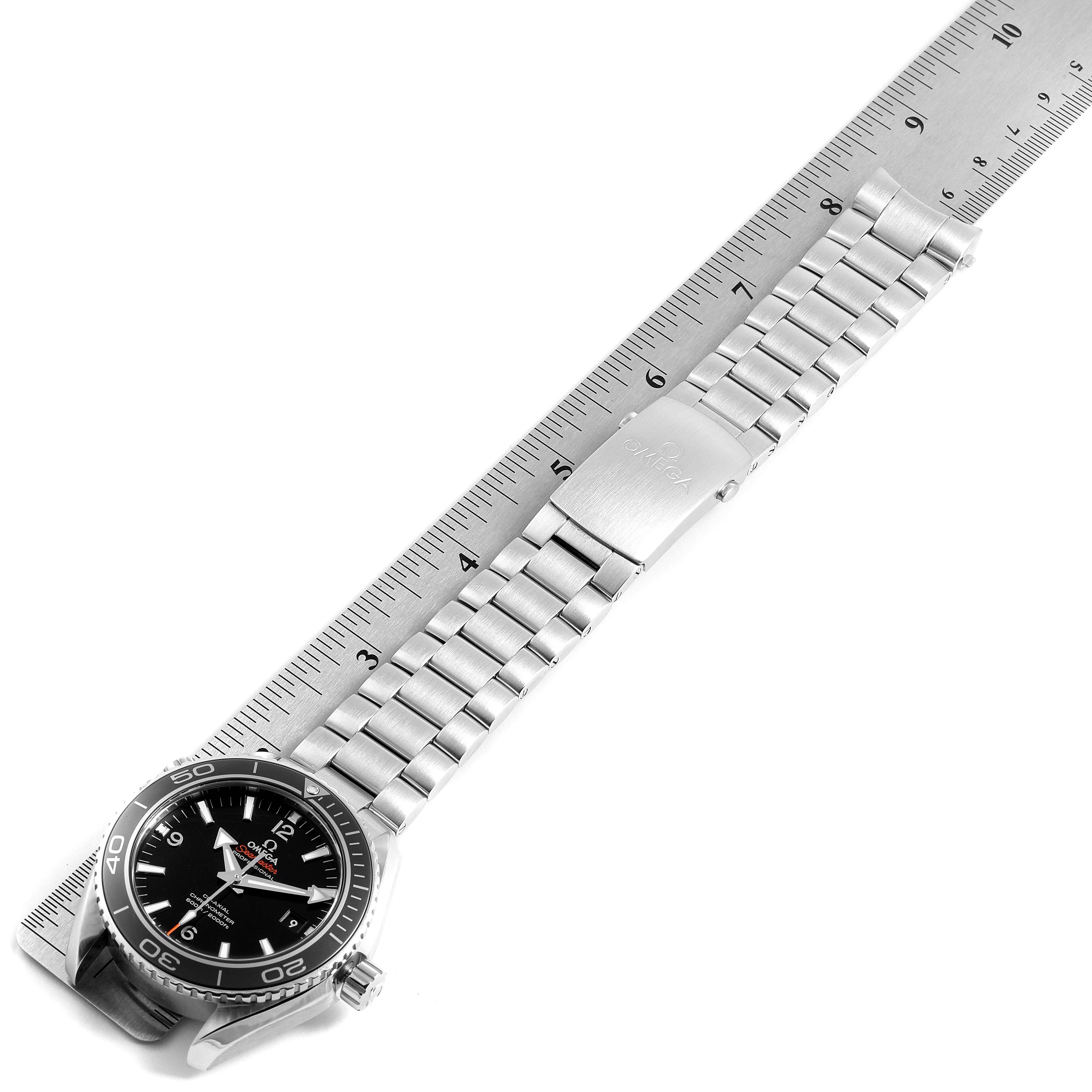 The image shows the Omega Planet Ocean 232.30.46.21.01.001 Men's Stainless Steel Black Dial 232.30.46.21.01.001 Men's Stainless Steel Black Dial watch laid flat with its face, stainless steel bracelet, and clasp visible alongside a ruler.
