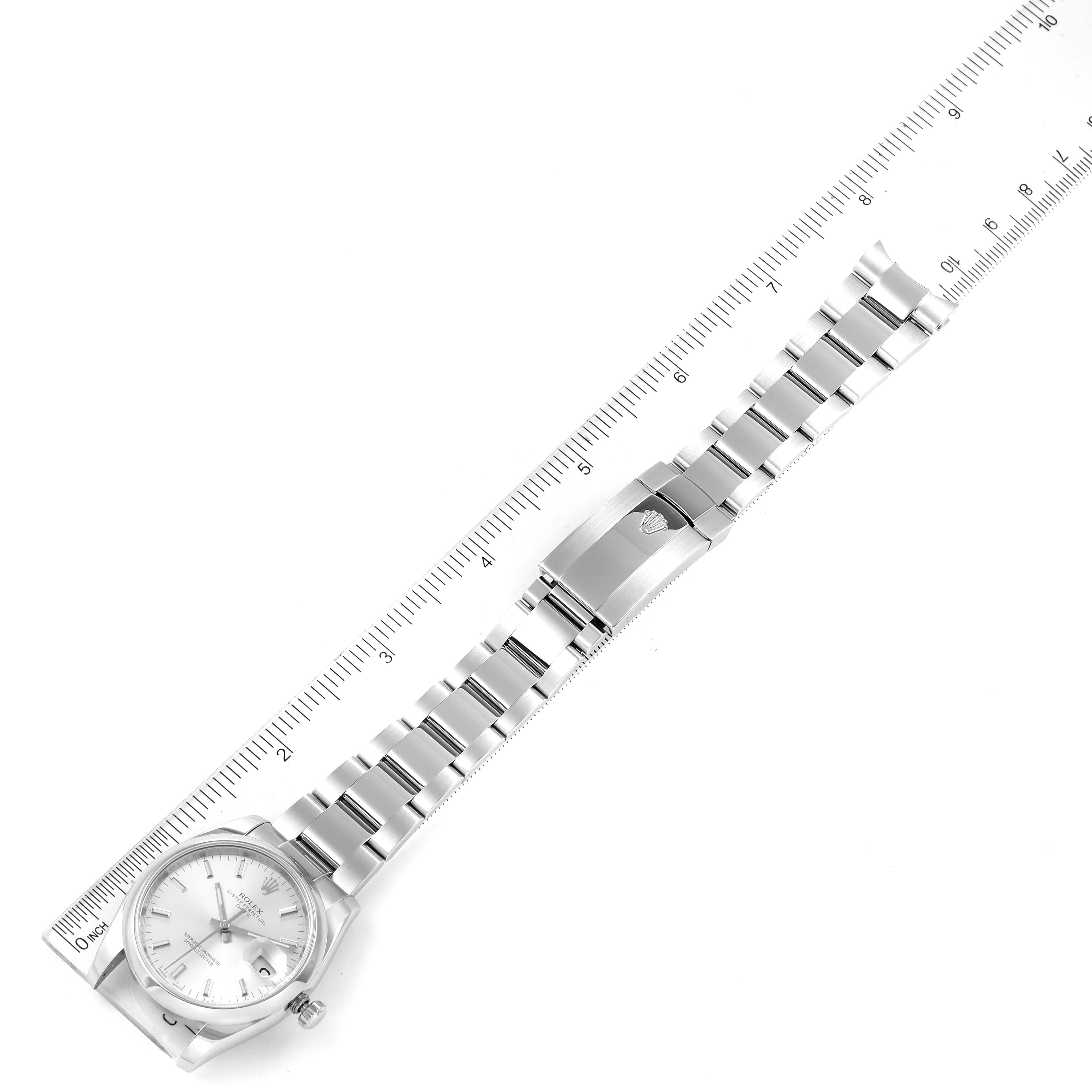 The image shows a top view of the Rolex Date 115200 Men's Stainless Steel Silver Dial 115200 Men's Stainless Steel Silver Dial model watch, including the face, band, and clasp, with a ruler beside it for scale.