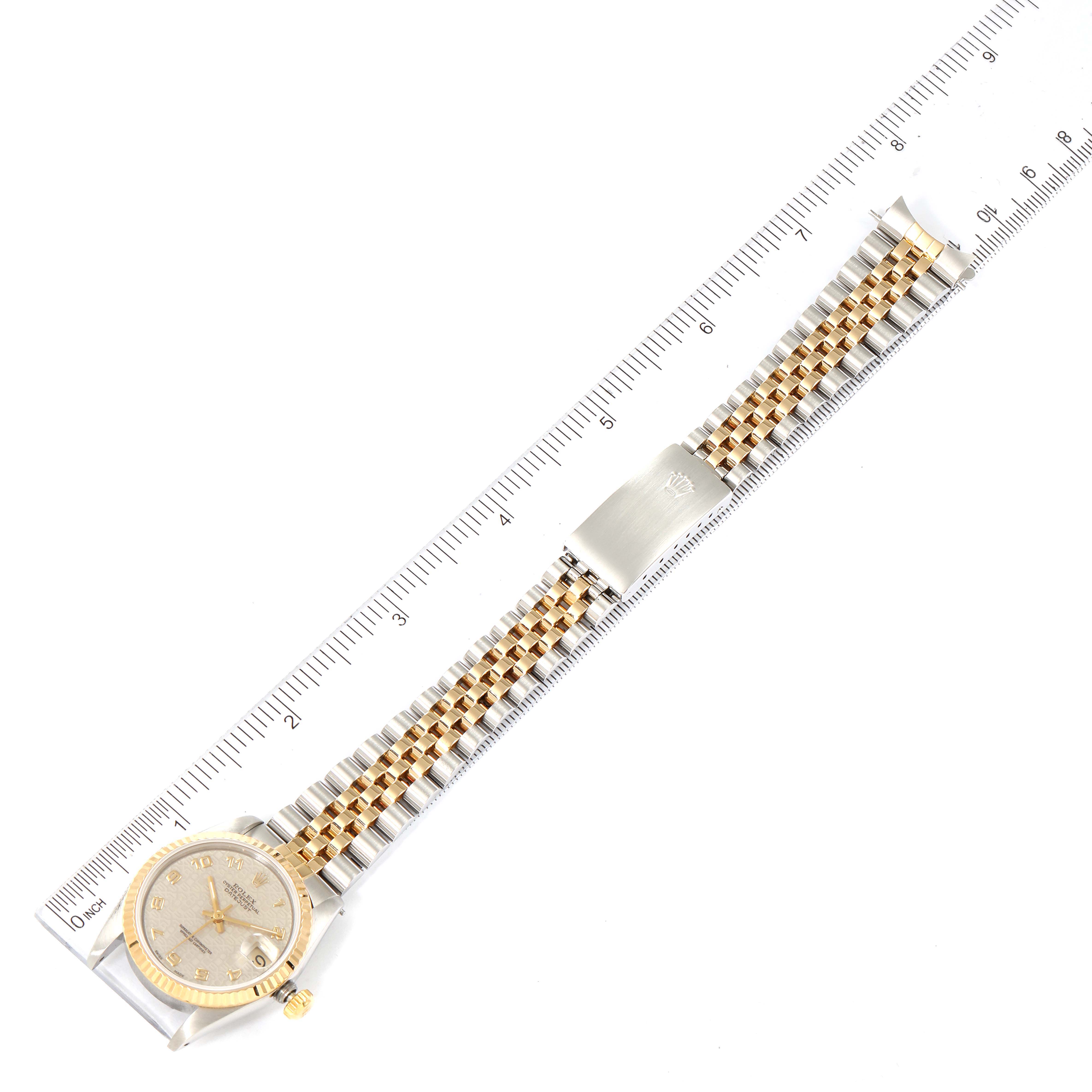 The image shows a top-down view of a Mid-Size Rolex watch, highlighting its gold and silver bracelet, face, and part of a ruler for scale.