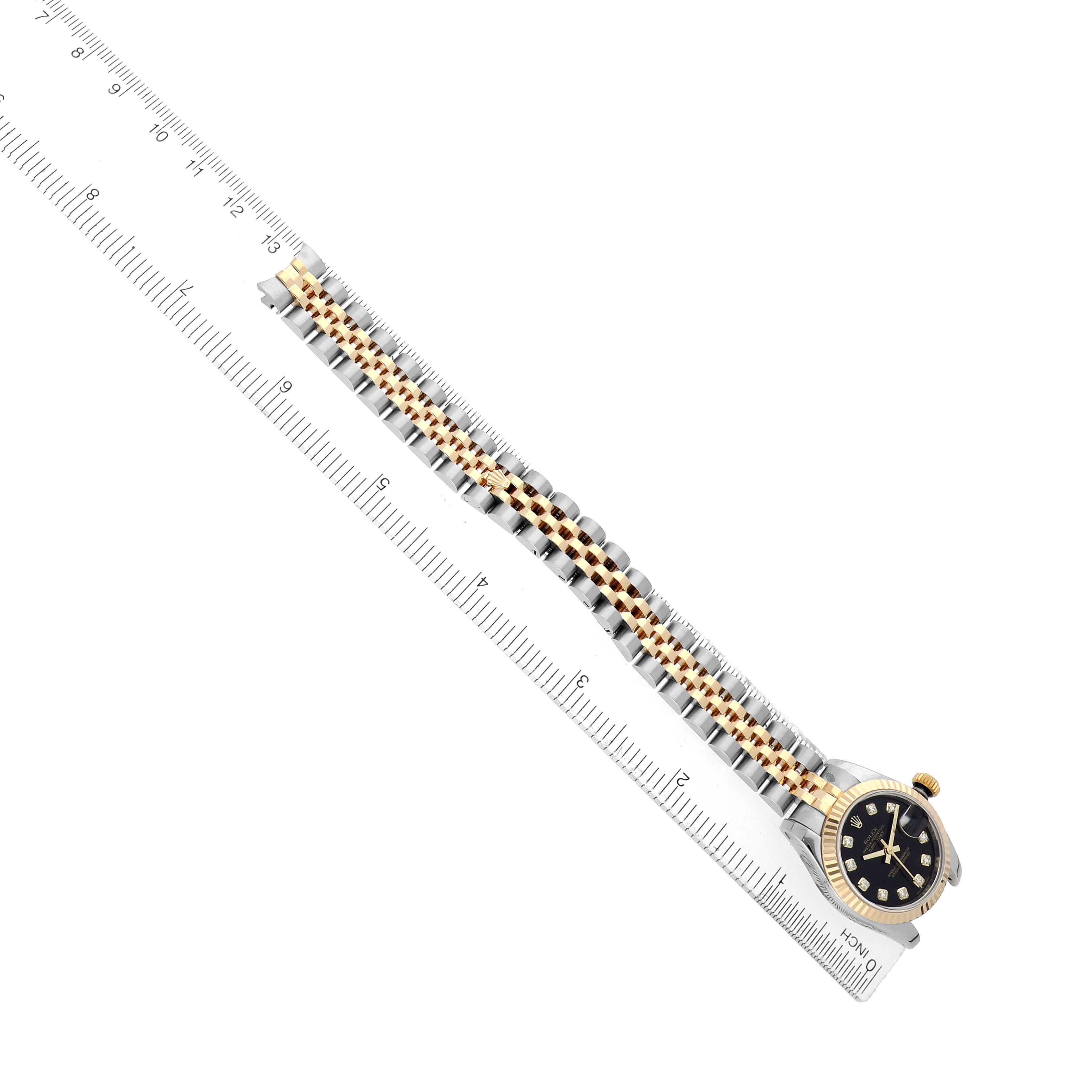 The Rolex Datejust 179173 Women's Steel and Gold (two tone) Black Dial watch is shown from an angled top view, highlighting the dial, bezel, and bracelet alongside a ruler.