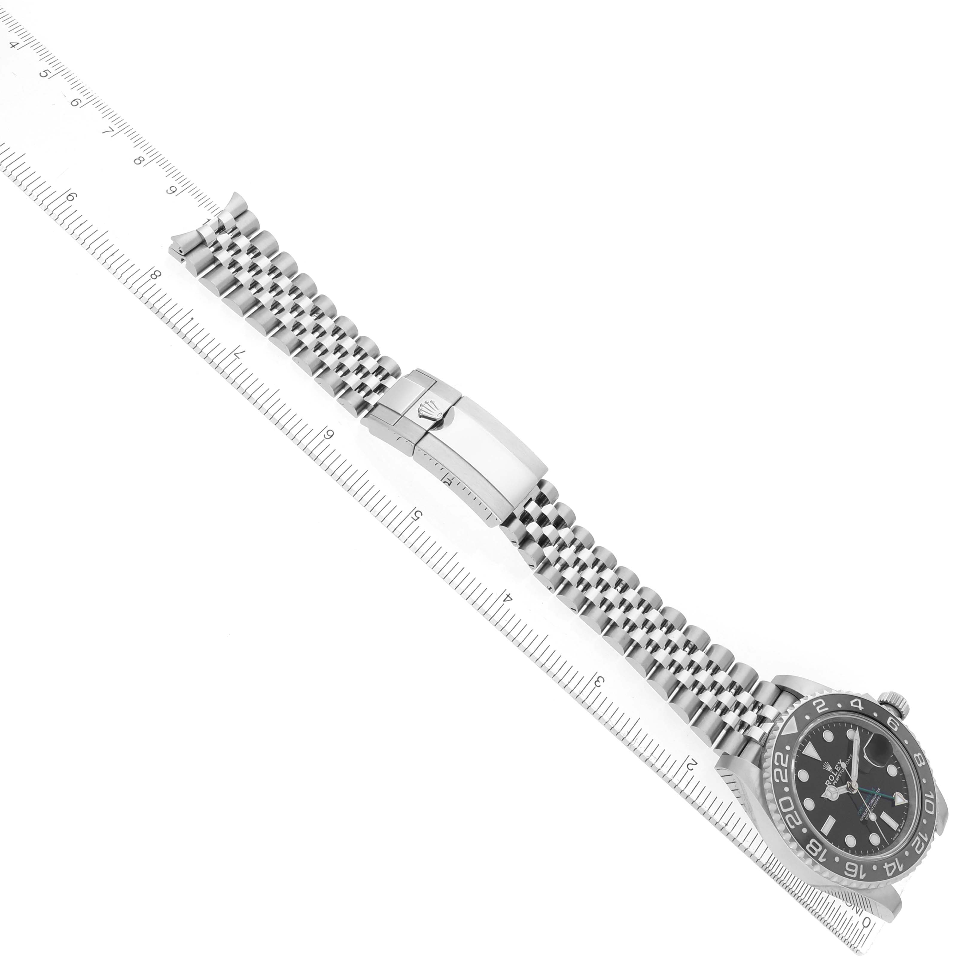 The Rolex GMT-Master 126710 Men
s Stainless Steel Black Dial watch is shown laid flat with the face, bracelet, and clasp visible, placed alongside a ruler for scale.