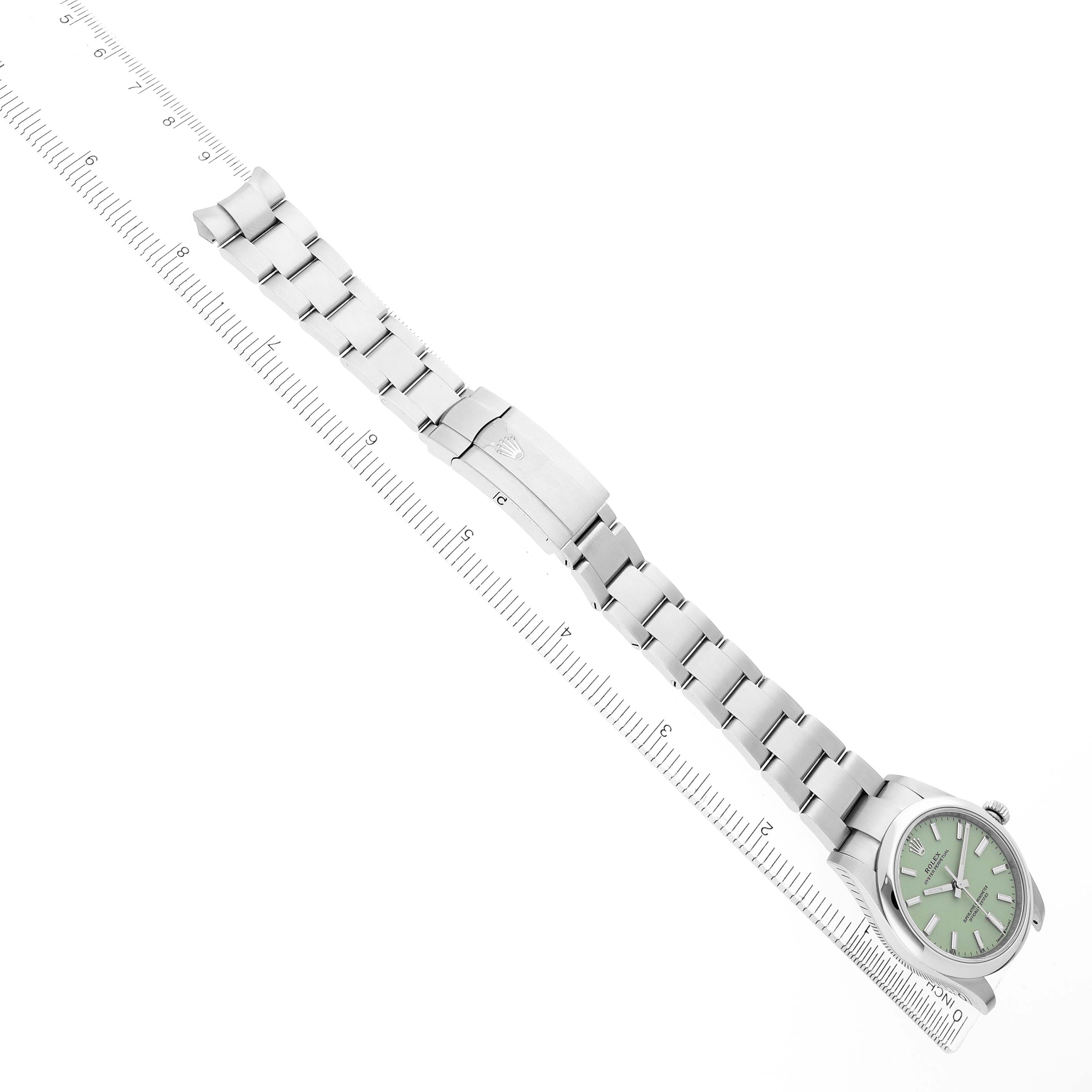 The Rolex Oyster Perpetual 124200 Men
s Stainless Steel Green Dial watch is shown diagonally, displaying its face, bracelet, and clasp next to a ruler for size reference.