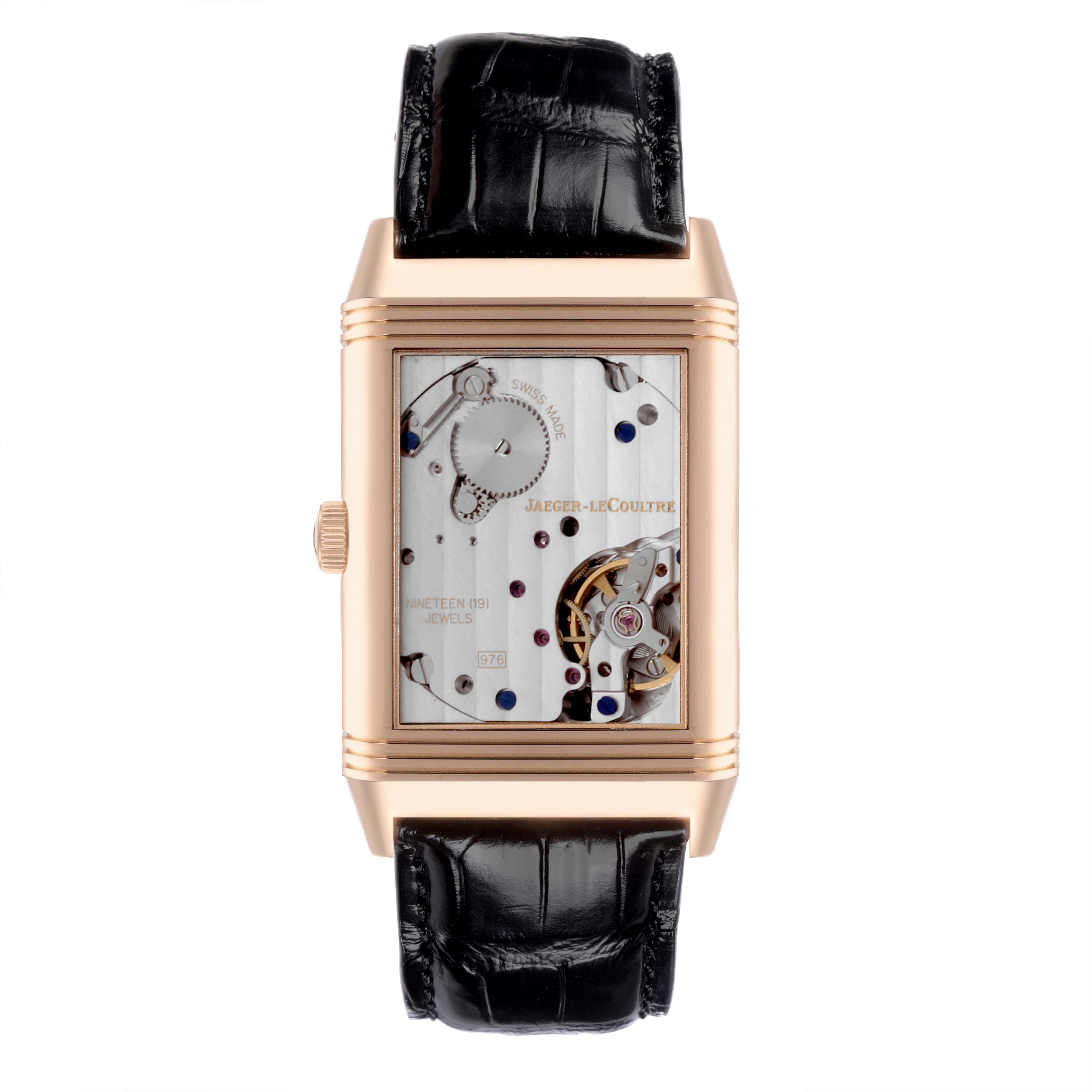 The Jaeger-LeCoultre Reverso watch is shown from a front angle, displaying its mechanical movement and leather strap.
