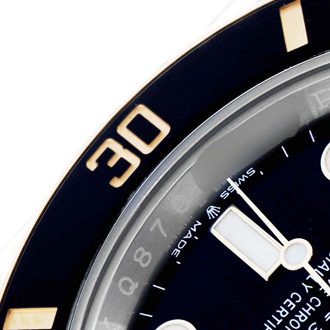 The image shows a close-up of the Rolex Submariner 126613 Men
s Steel and Gold (two tone) Black Dial
s bezel and a portion of the dial with indices and the minute hand.