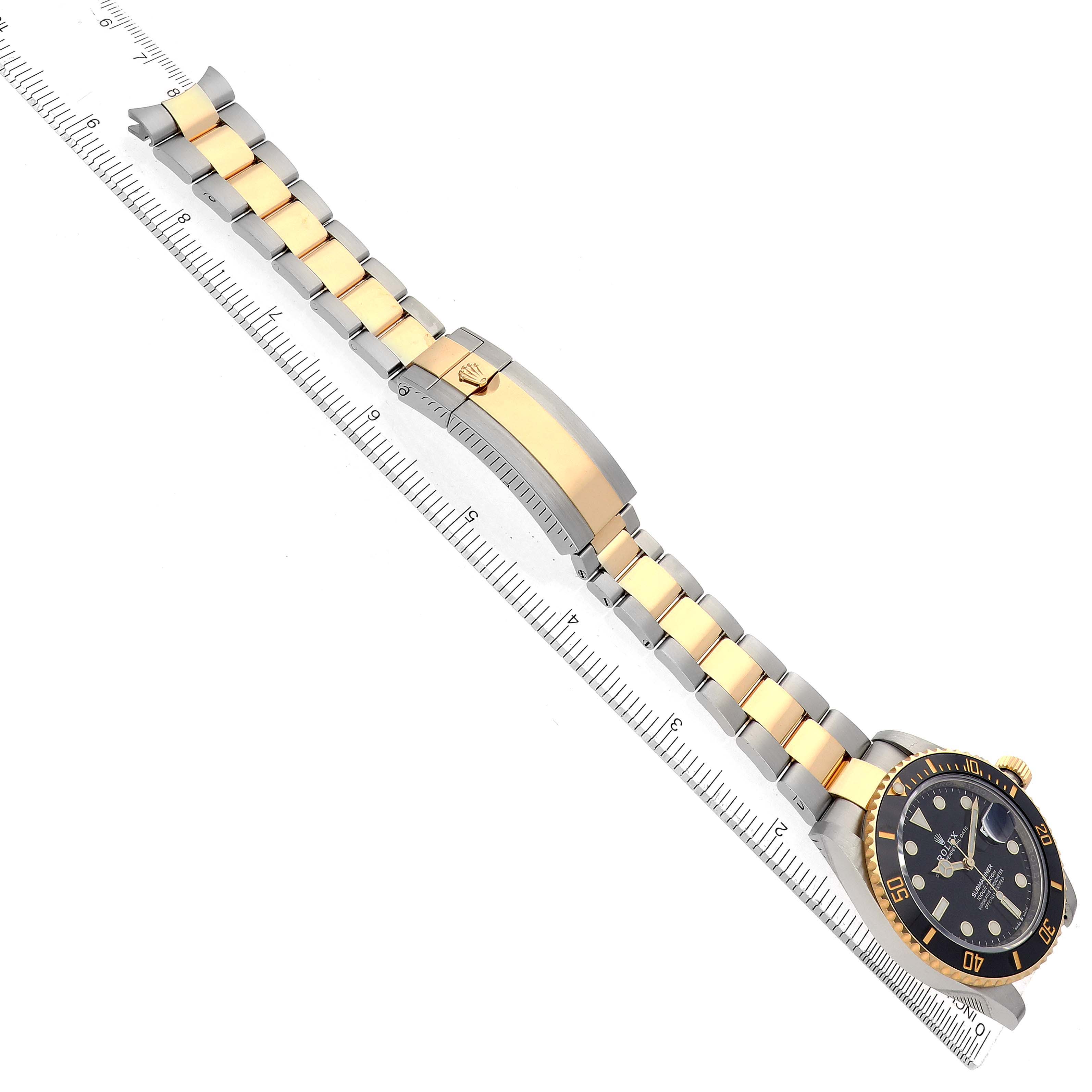 The image shows a Rolex Submariner 126613 Men
s Steel and Gold (two tone) Black Dial watch laid flat, showcasing the face and full bracelet on a ruler.