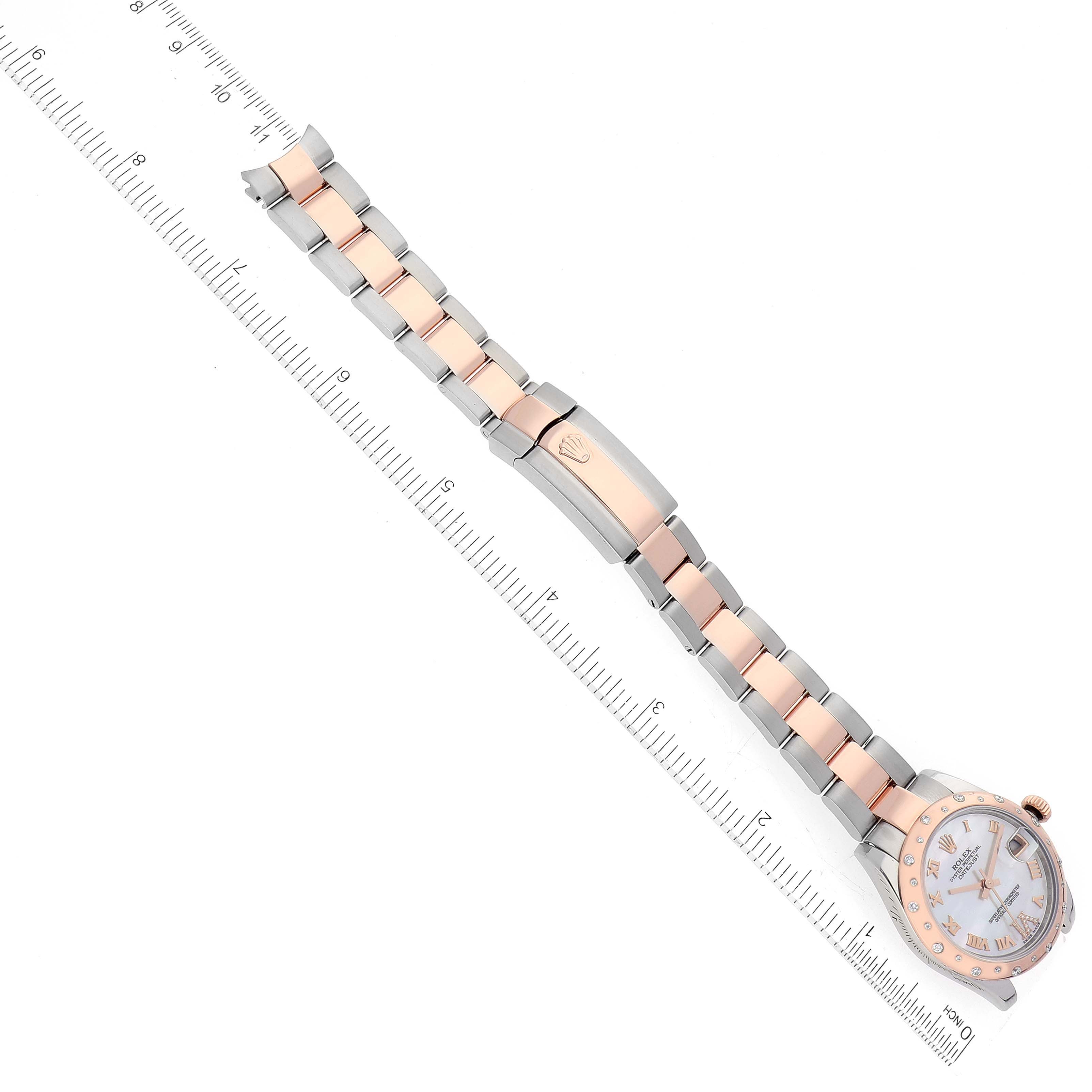 This image shows a Rolex Mid-Size 178341 Women
s Steel and Gold (two tone) Mother of Pearl Dial 178341 Women
s Steel and Gold (two tone) Mother of Pearl Dial model watch from a top-down angle, displaying its bracelet, clasp, and face next to a ruler.