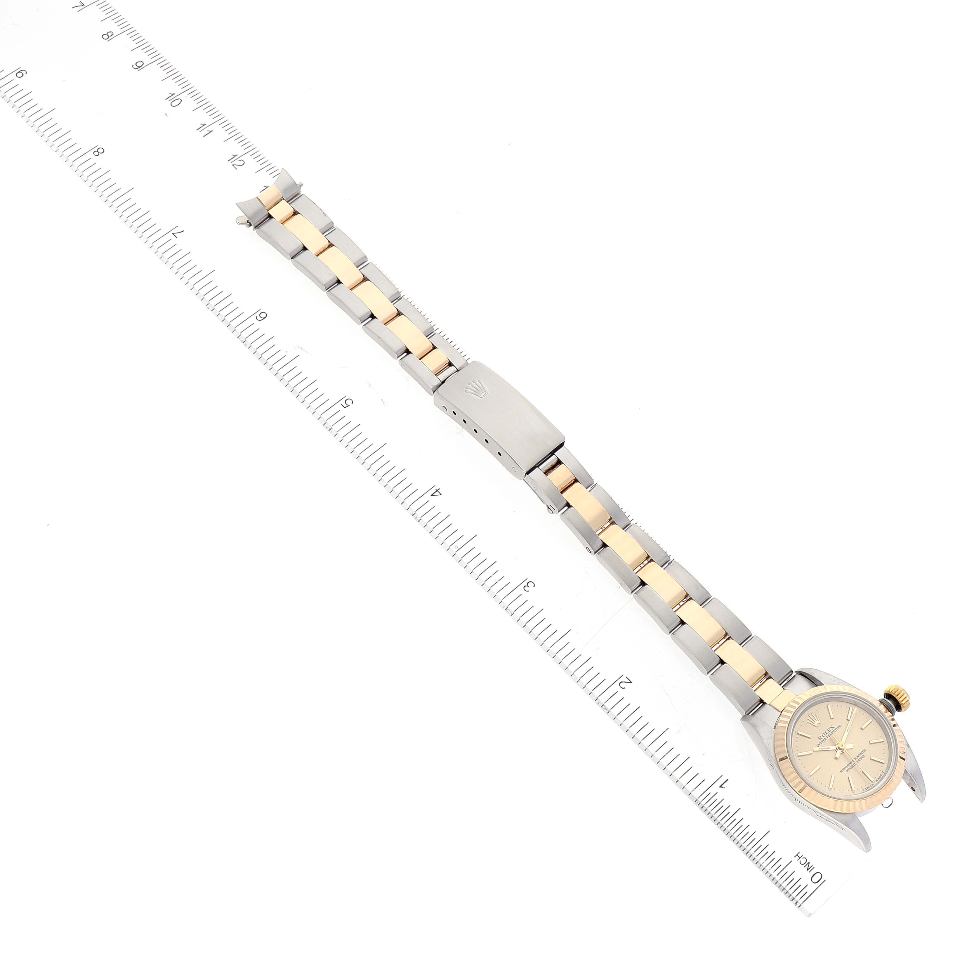 This image shows a top-down view of a Rolex Oyster Perpetual 67193 Women's Steel and Gold (two tone) Champagne Dial 67193 Women's Steel and Gold (two tone) Champagne Dial watch and a ruler, highlighting its bracelet and face.