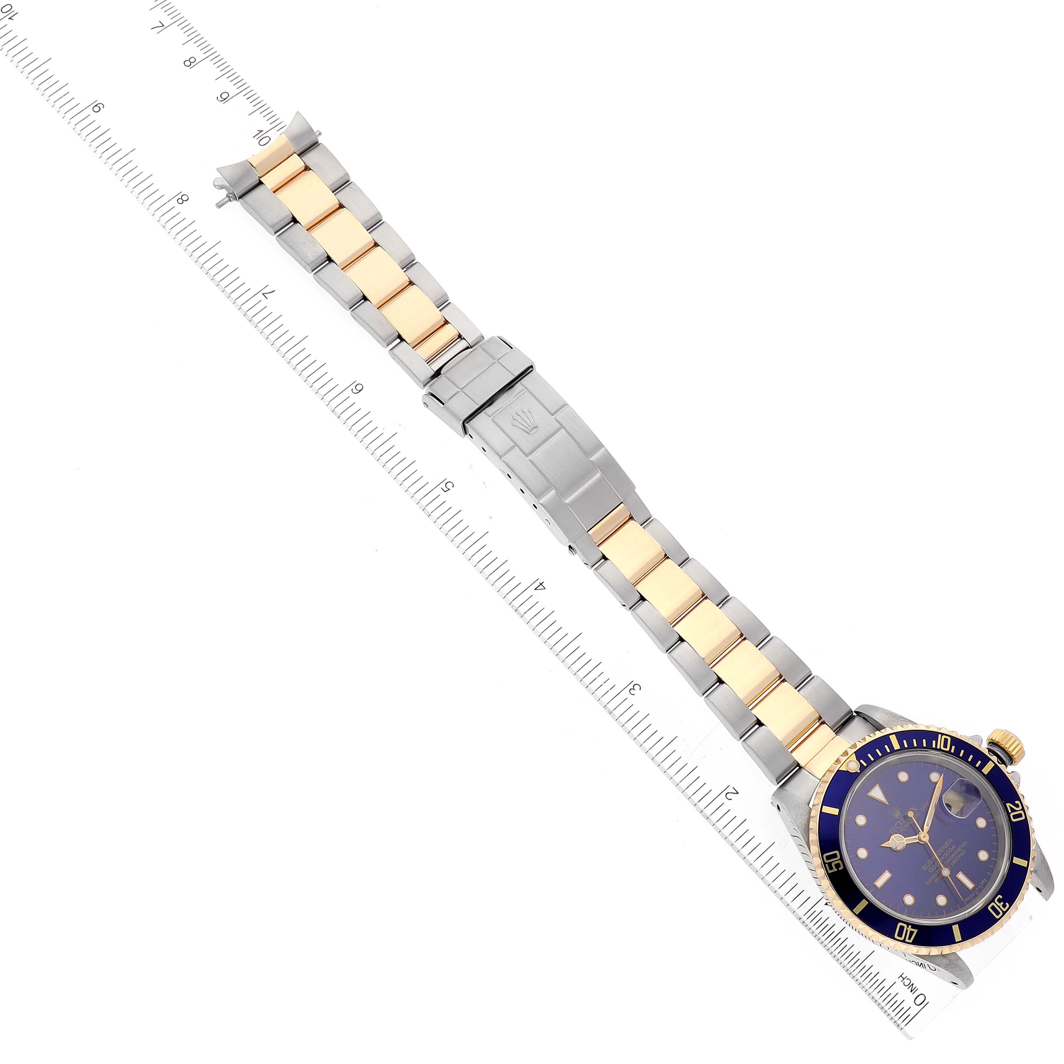 The image shows a top view of a Rolex Submariner 16613 Men's Steel and Gold (two tone) Blue Dial 16613 Men's Steel and Gold (two tone) Blue Dial watch, displaying the face, bezel, and full two-tone bracelet against a ruler background.