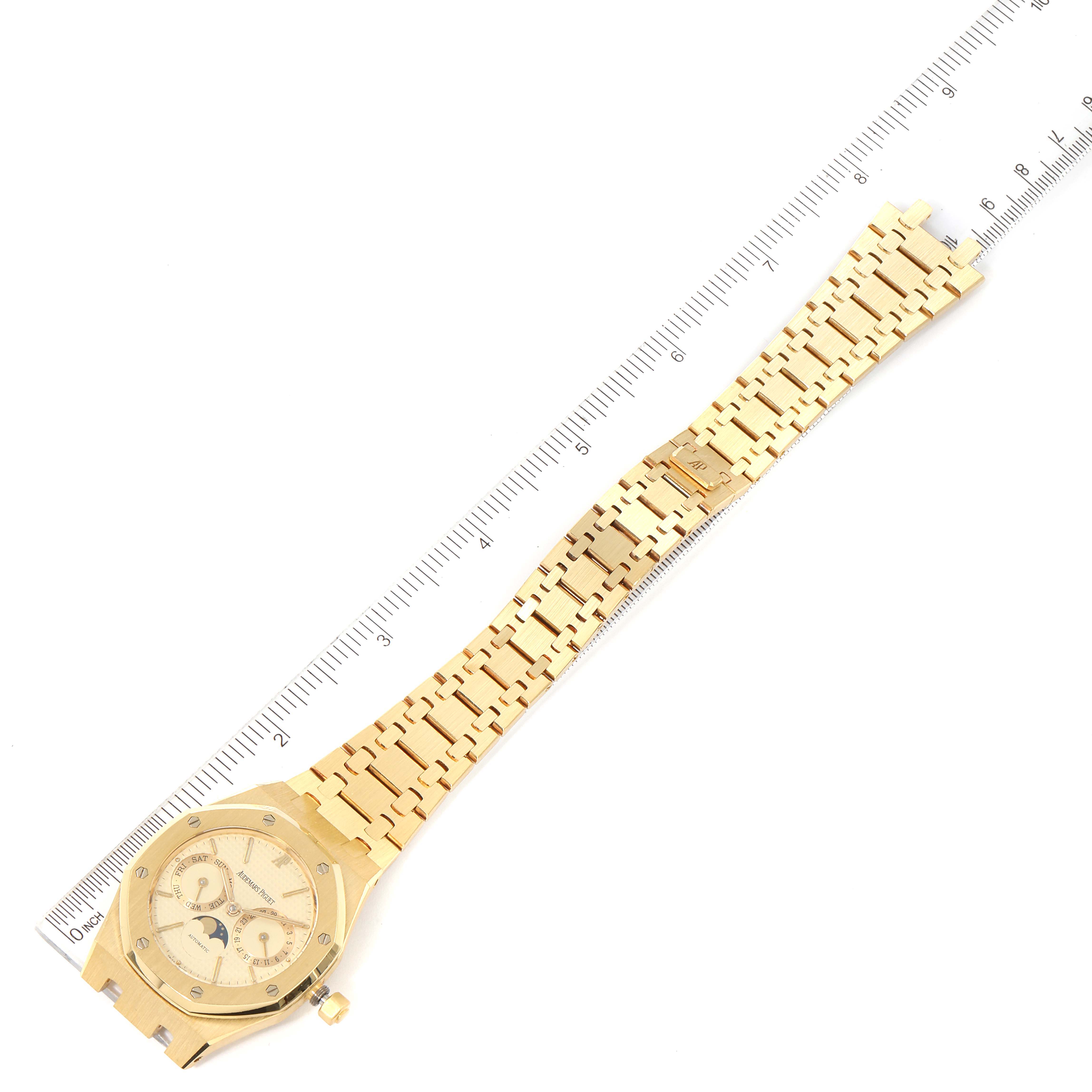 The image shows an overhead view of an Audemars Piguet Royal Oak 25594BA.OO.0477BA.01 Men's Yellow Gold Champagne Dial 25594BA.OO.0477BA.01 Men's Yellow Gold Champagne Dial watch, depicting its gold bracelet and watch face next to a ruler.