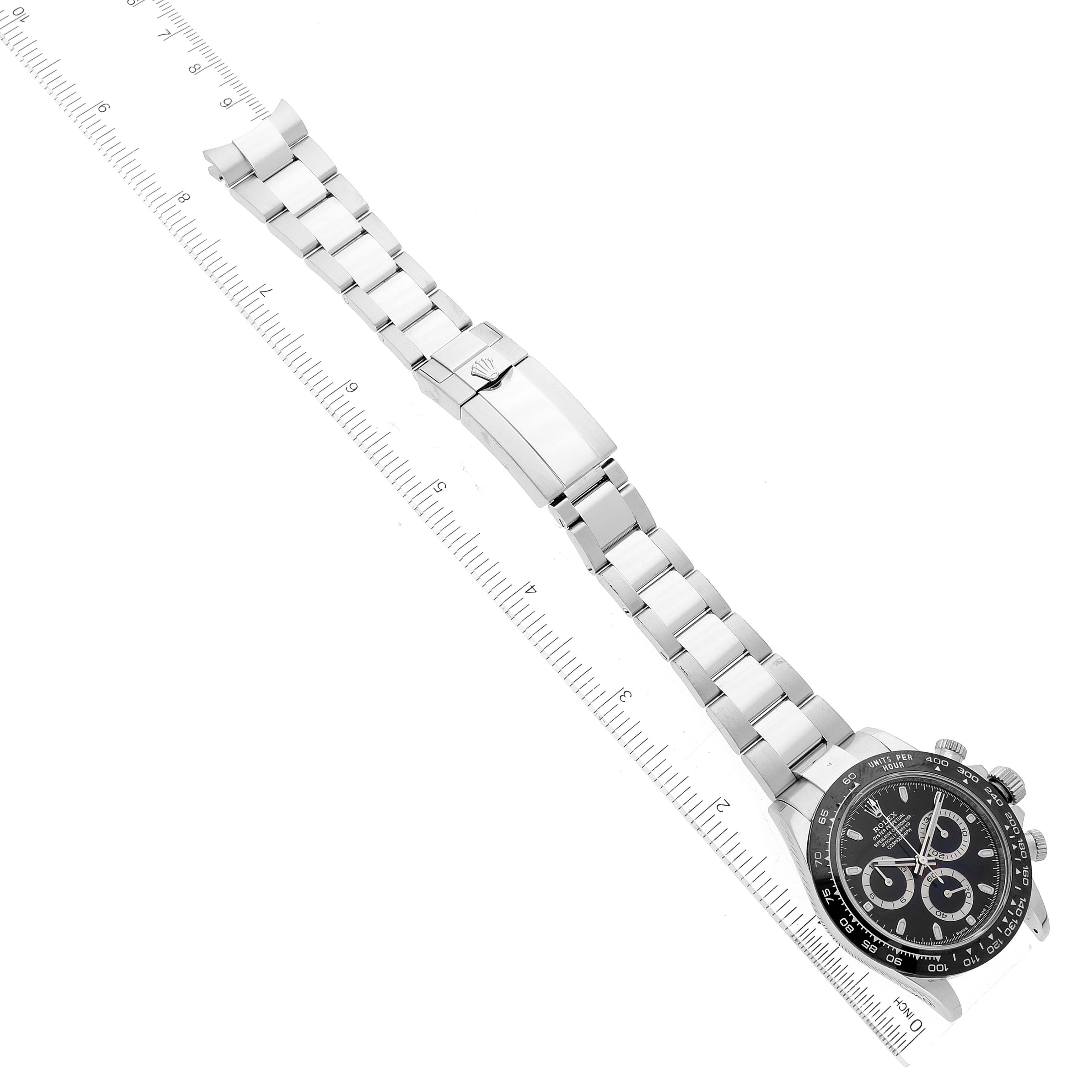 The image shows an overhead view of a Rolex Daytona 116500 Men's Stainless Steel Black Dial 116500 Men's Stainless Steel Black Dial watch and its metal bracelet, aligned with a ruler.