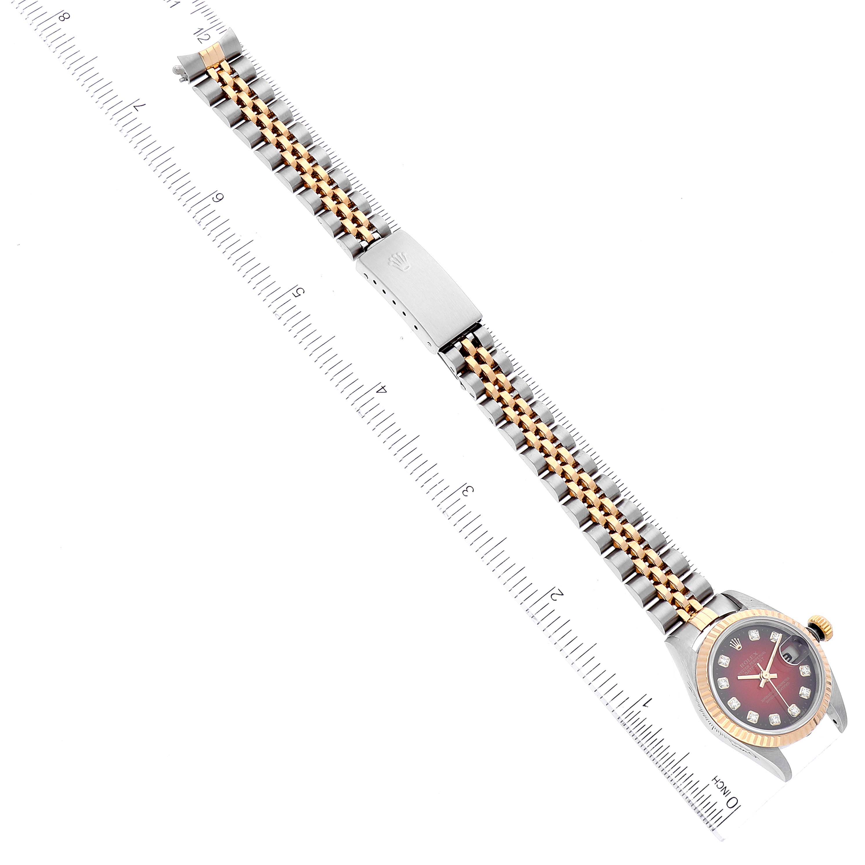 The image shows a Rolex Datejust 79173 Women
s Steel and Gold (two tone) Red Dial 79173 Women
s Steel and Gold (two tone) Red Dial watch laid flat next to a ruler, displaying the full bracelet and dial from above.