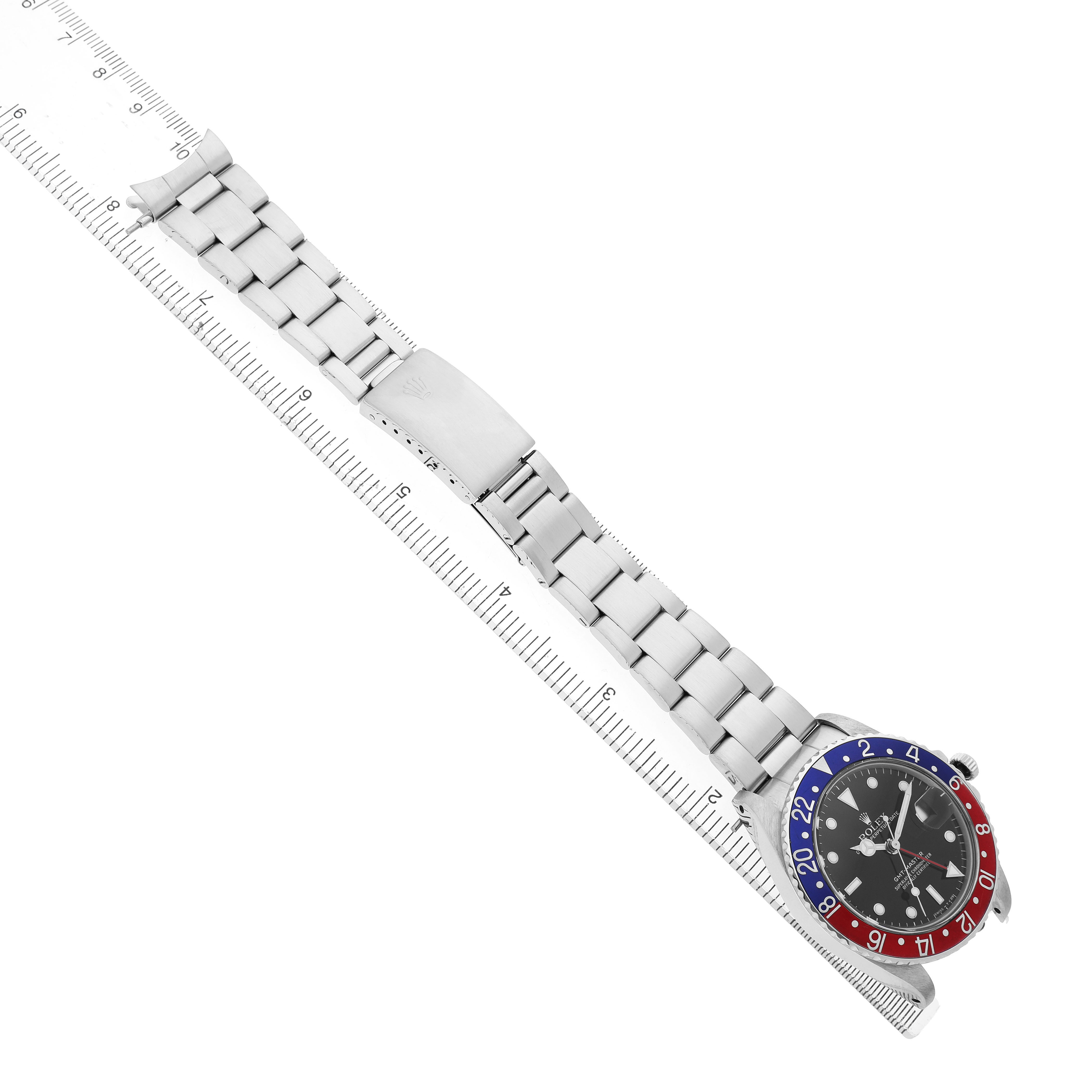 The Rolex GMT-Master 16750 Men's Stainless Steel Black Dial watch is shown from a top-down angle, displaying the bezel, dial, and full bracelet alongside a ruler.
