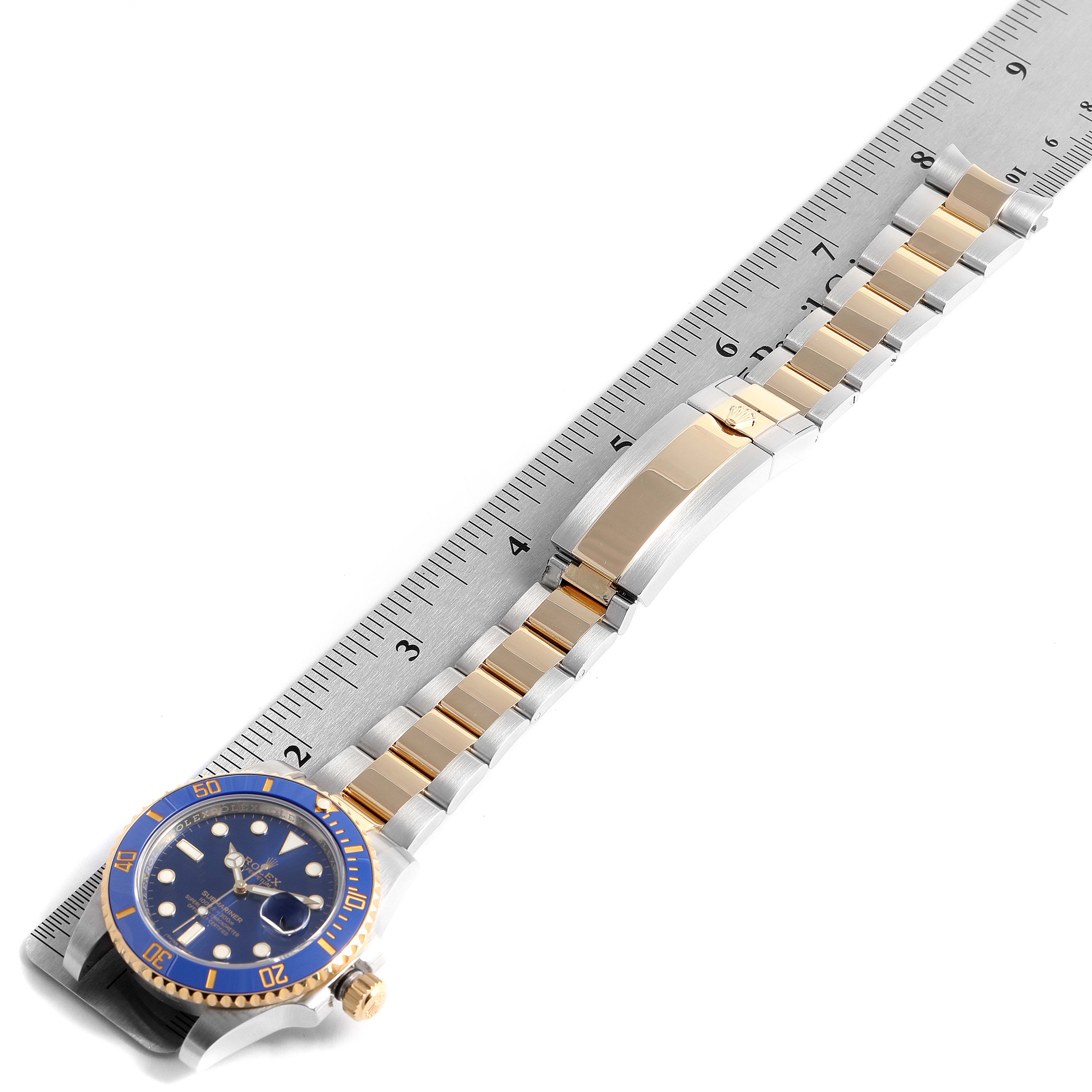 The image shows a Rolex Submariner 116613 Men's Steel and Gold (two tone) Blue Dial 116613 Men's Steel and Gold (two tone) Blue Dial watch, highlighting the face, bezel, and metal strap alongside a measuring scale.