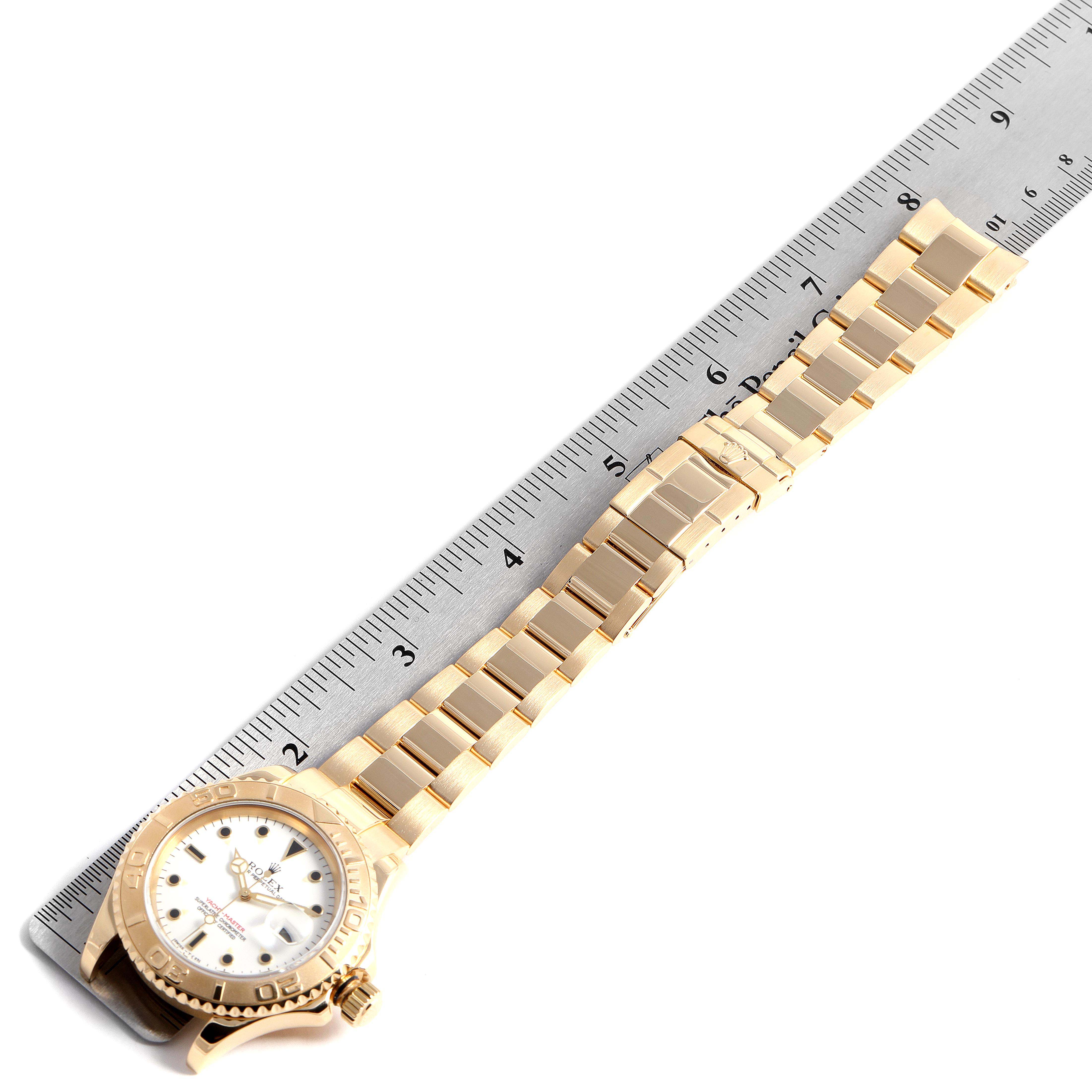 The Rolex Yacht-Master 16628B Men's Yellow Gold White Dial 16628B Men's Yellow Gold White Dial watch is pictured with its full gold band laid out alongside a ruler.