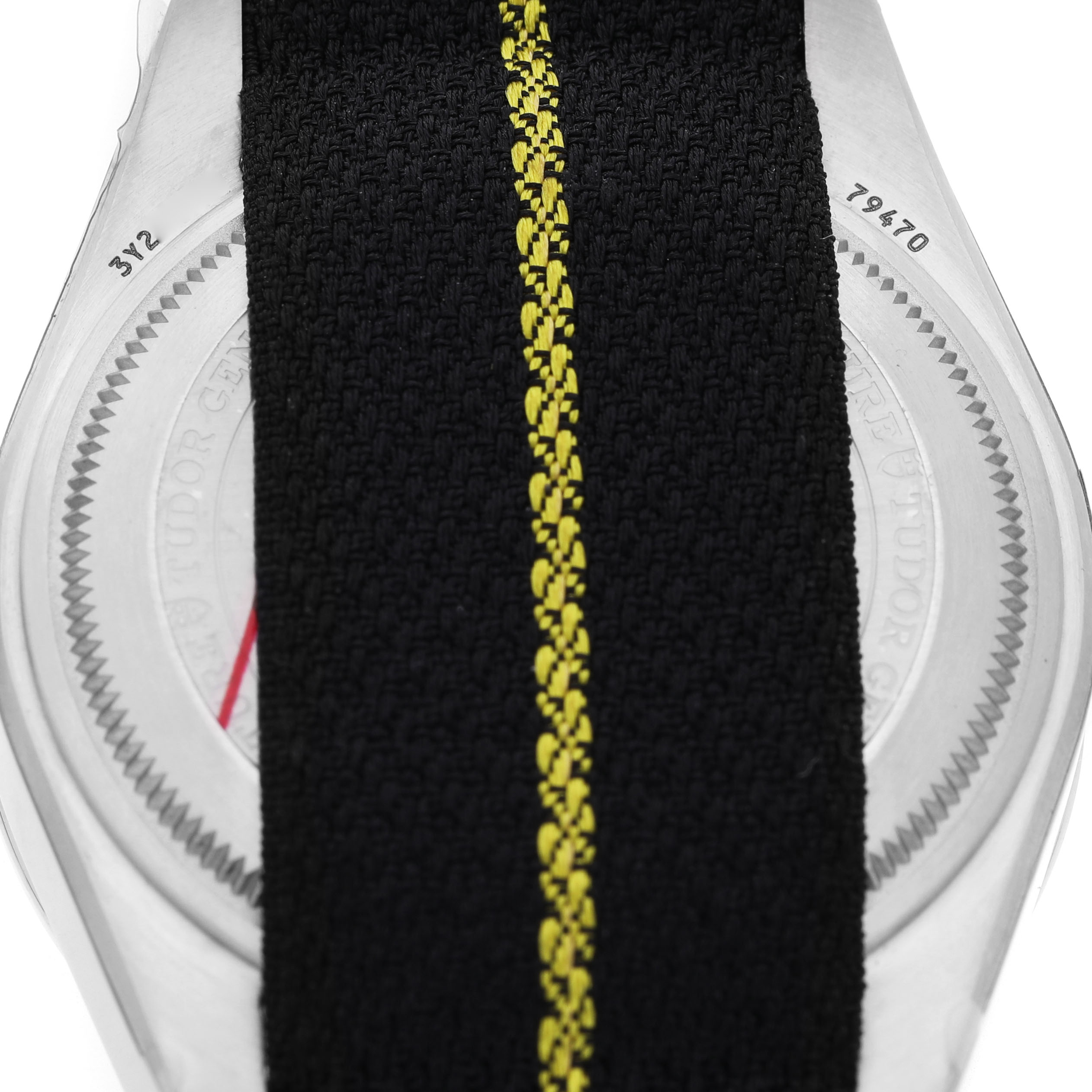 The image shows the back of the Tudor Heritage Black Bay 79470 Men's Stainless Steel Black Dial watch with a black fabric strap featuring a yellow stripe.