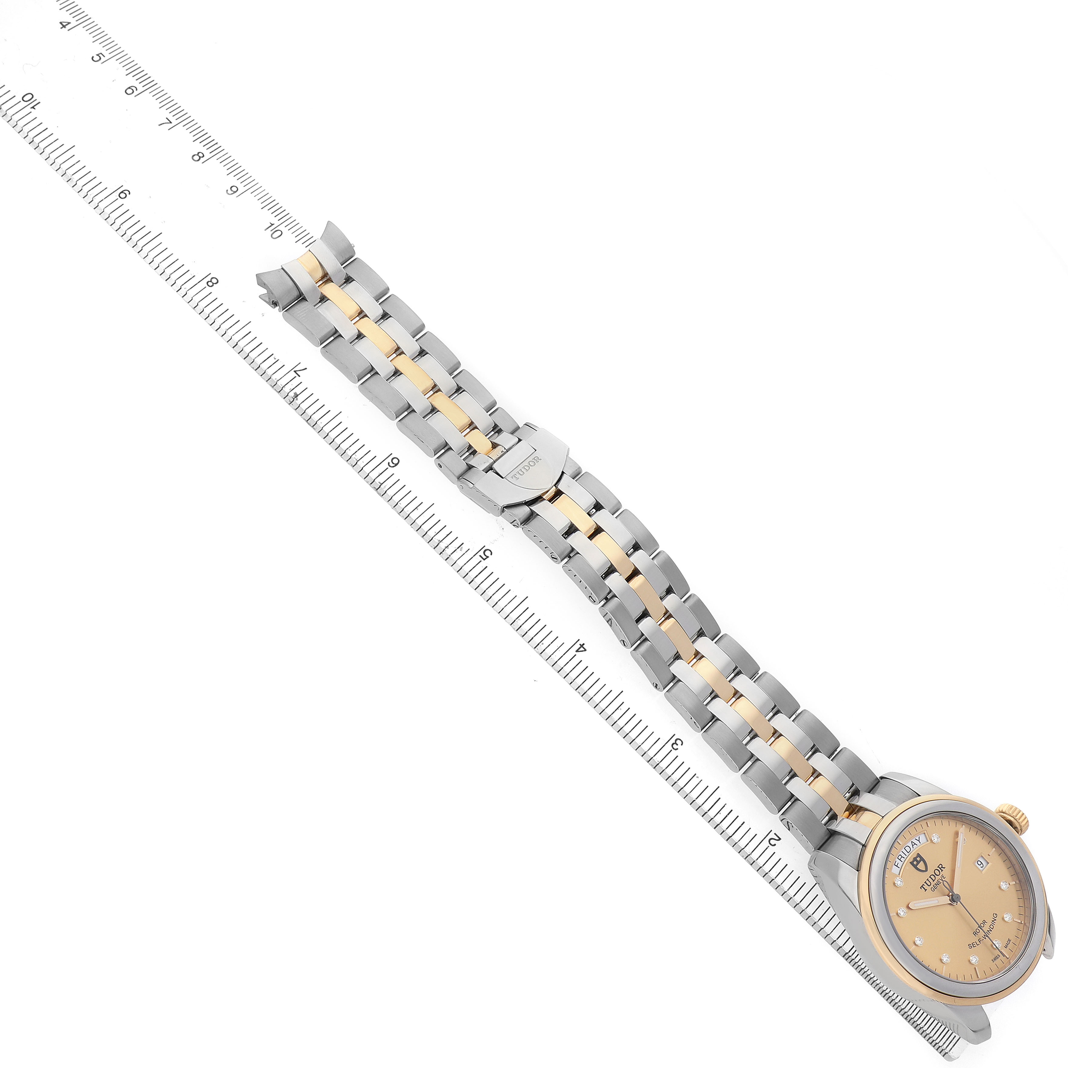 The Tudor Glamour 56003 Men's Steel and Gold (two tone) Champagne Dial watch is shown from an angled top view, highlighting its face, bracelet, and clasp aligned with a ruler.