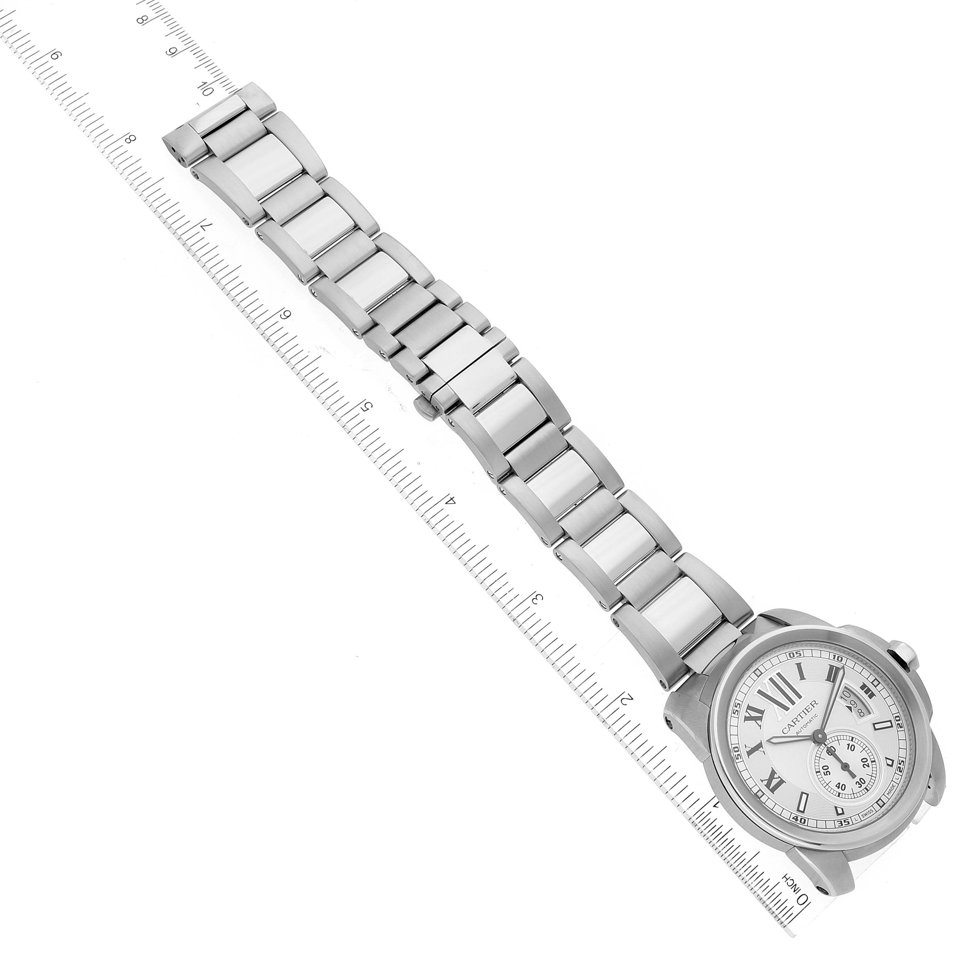 The image shows the face and bracelet of the Calibre de Cartier watch by Cartier, positioned against a ruler for scale.