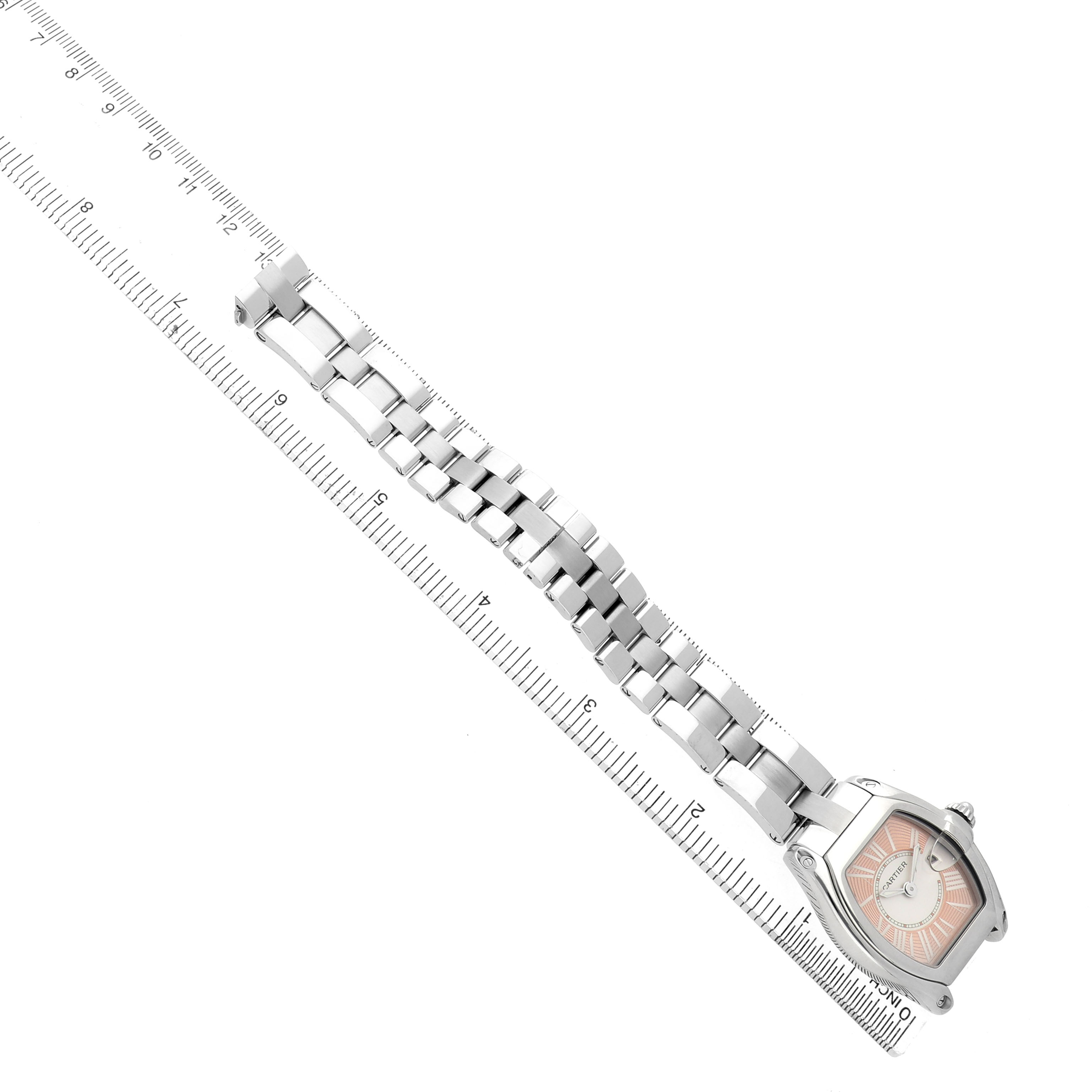 The Cartier Roadster W62017V3 Women's Stainless Steel Pink Dial watch is shown at an angle, displaying its case, dial, and full metal bracelet alongside a ruler.