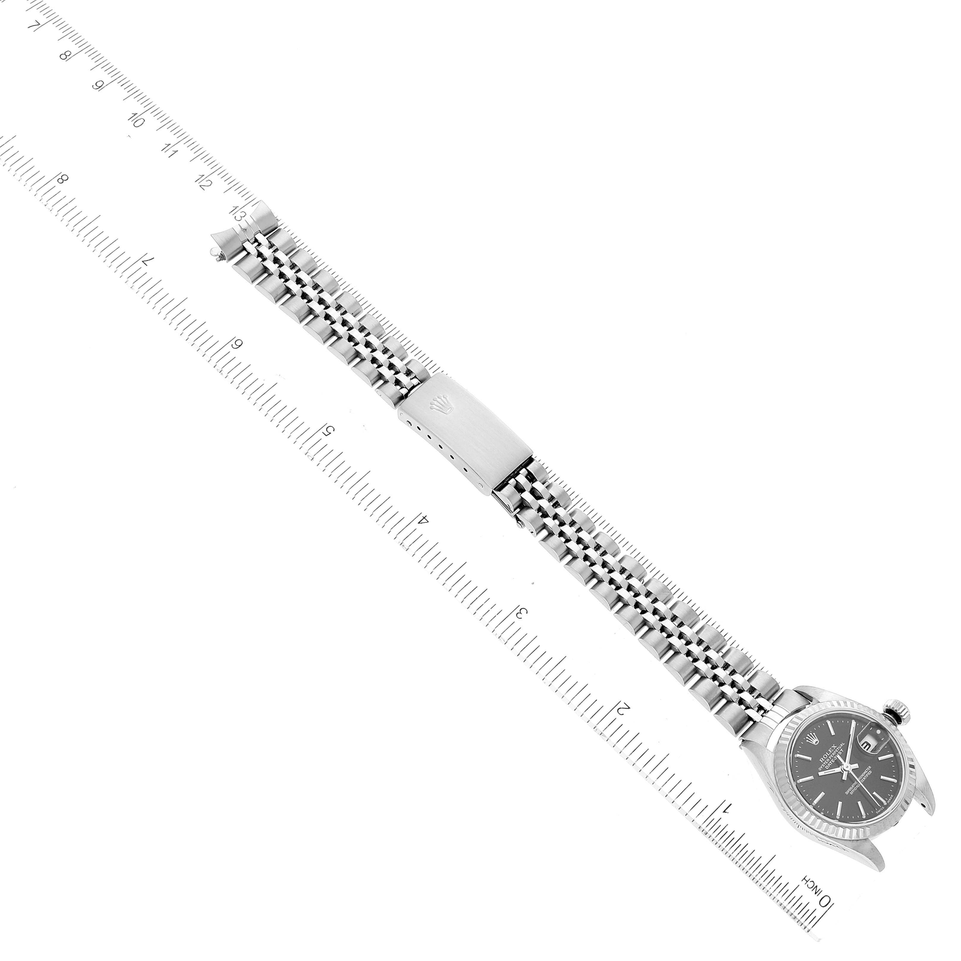 The image shows a top-down view of a Rolex Datejust 79174 Women
s Stainless Steel Black Dial 79174 Women
s Stainless Steel Black Dial watch with the full bracelet and clasp, placed next to a metric ruler.