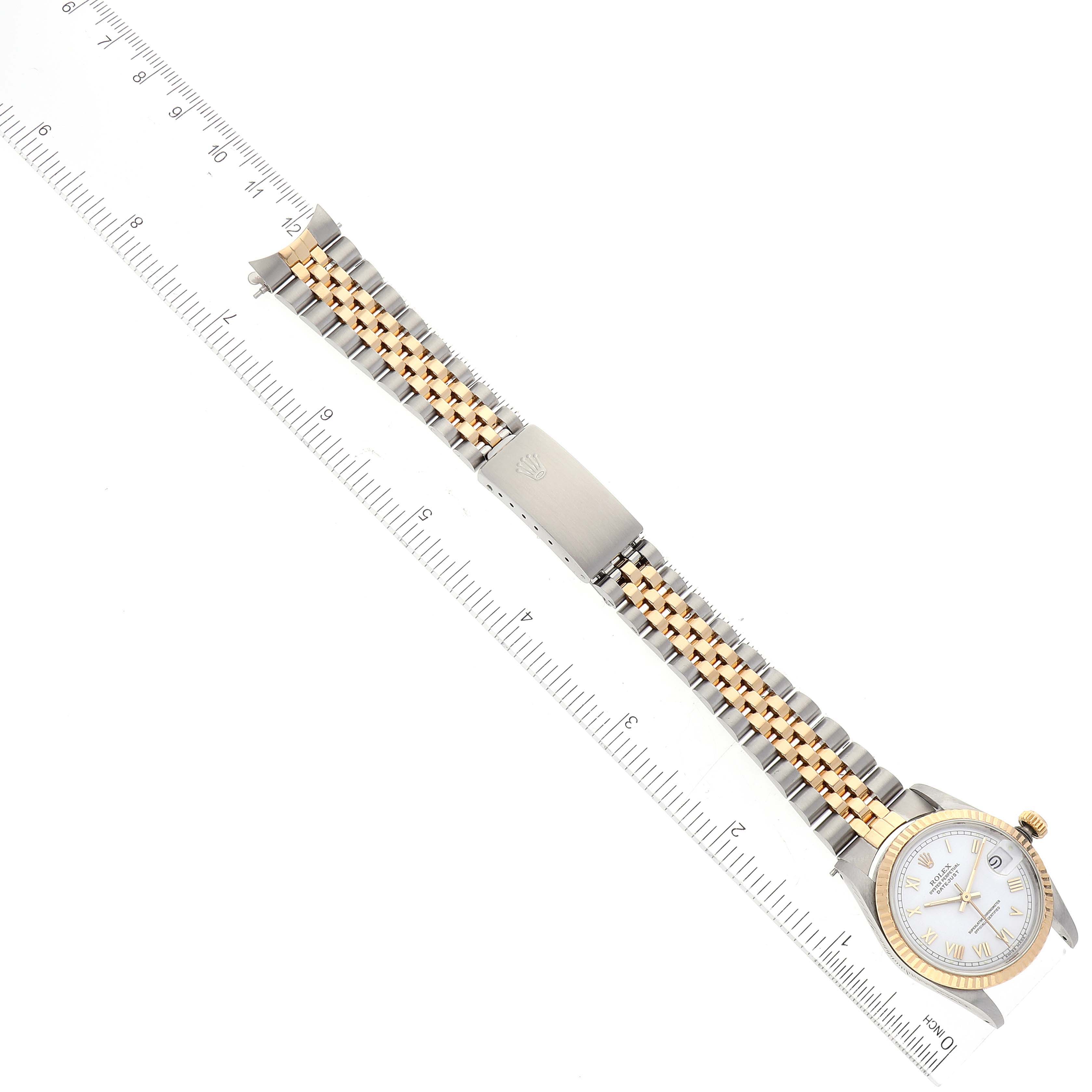The image shows a top-down view of a Rolex Mid-Size 68273 Women
s Steel and Gold (two tone) White Dial 68273 Women
s Steel and Gold (two tone) White Dial watch, highlighting its face, bezel, bracelet, clasp, and a measuring scale.
