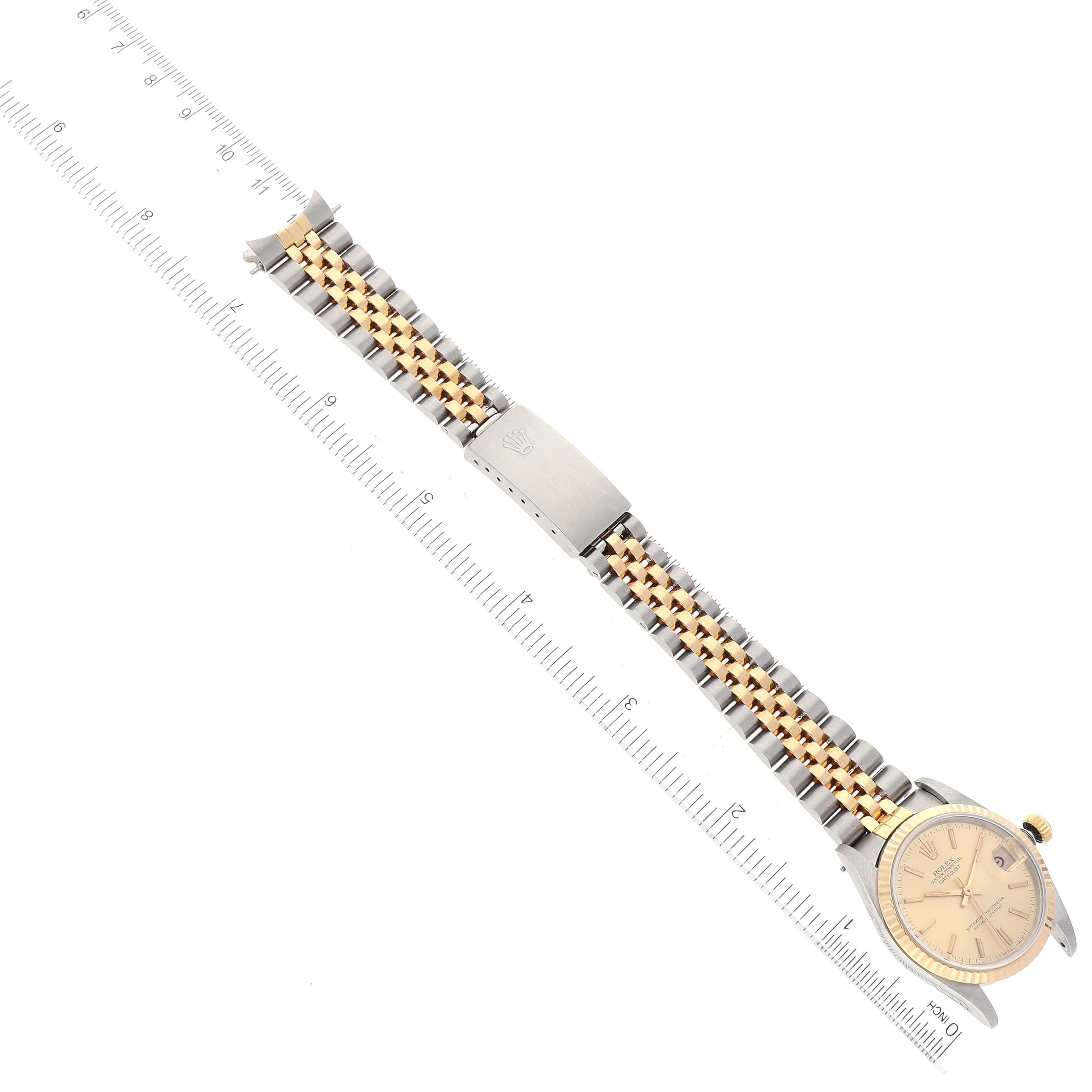 The image shows a top-down view of a Rolex Mid-Size 68273 Women
s Steel and Gold (two tone) Champagne Dial 68273 Women
s Steel and Gold (two tone) Champagne Dial watch, highlighting the face, crown, and two-tone bracelet with a ruler for scale.