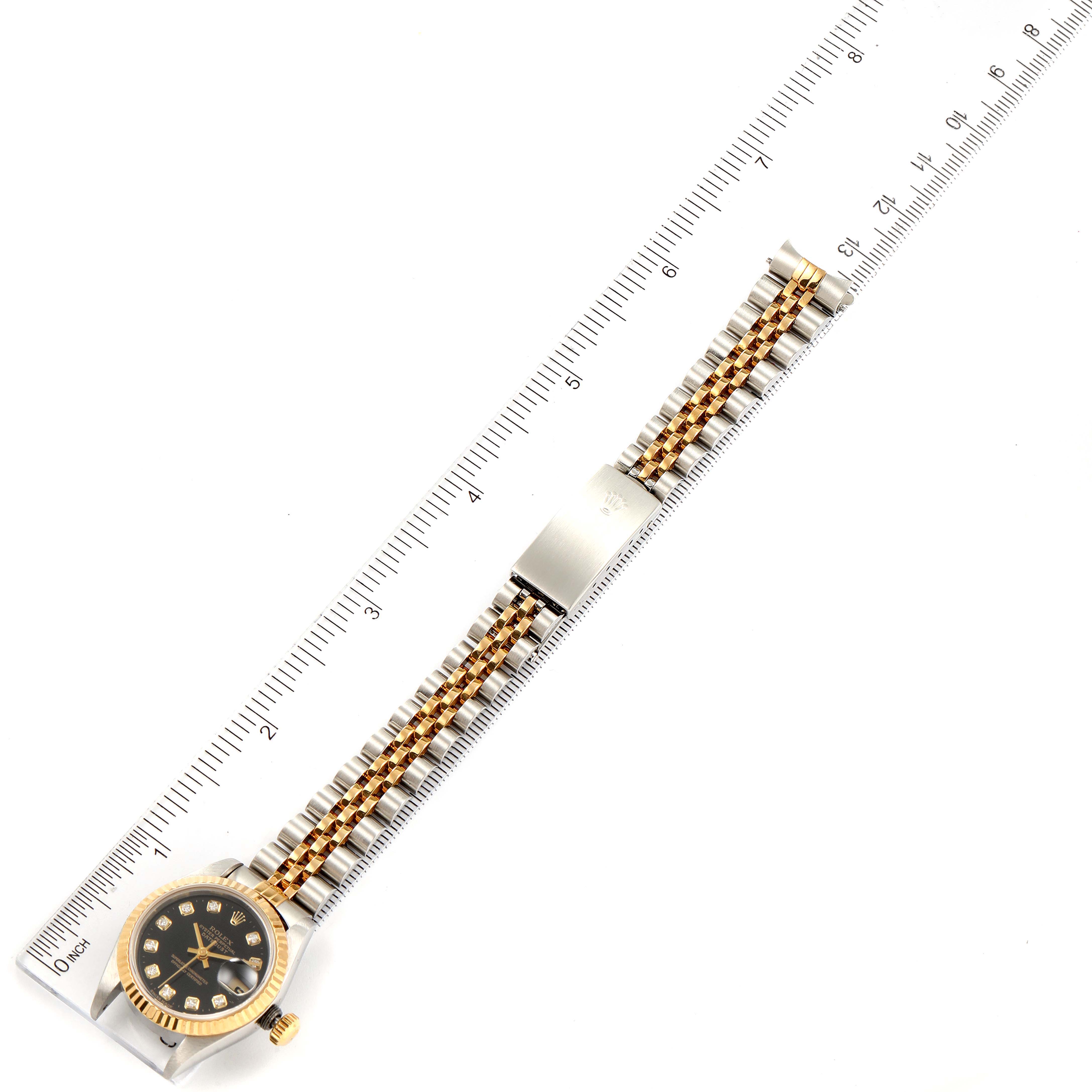The image shows a Rolex Datejust 79173 Women
s Steel and Gold (two tone) Black Dial 79173 Women
s Steel and Gold (two tone) Black Dial watch laid flat with a ruler beside it, displaying the entire watch from dial to clasp.