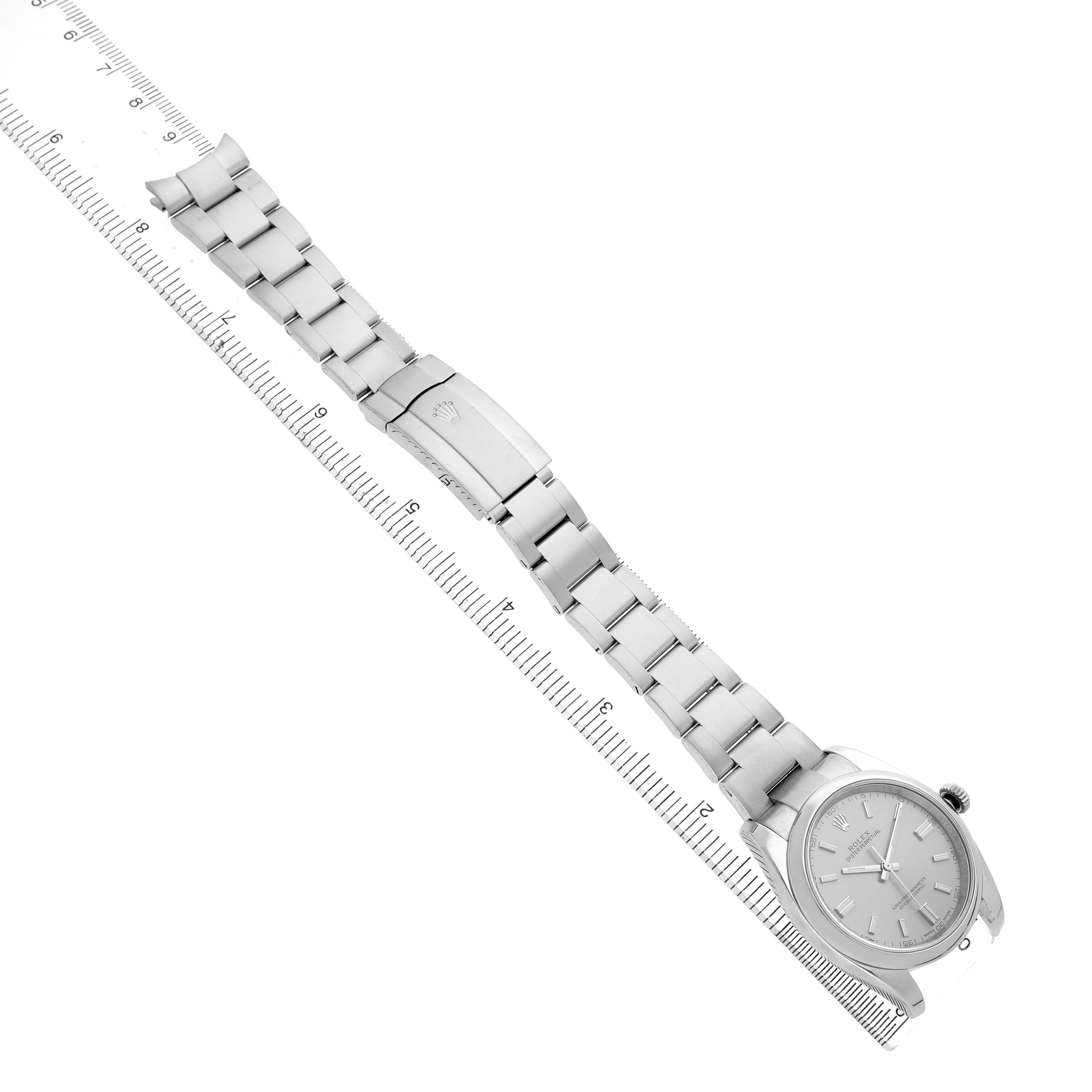 The Rolex Oyster Perpetual 116000 Men's Stainless Steel Silver Dial watch is shown from an angled overhead view with its full bracelet and clasp visible, along with a ruler.