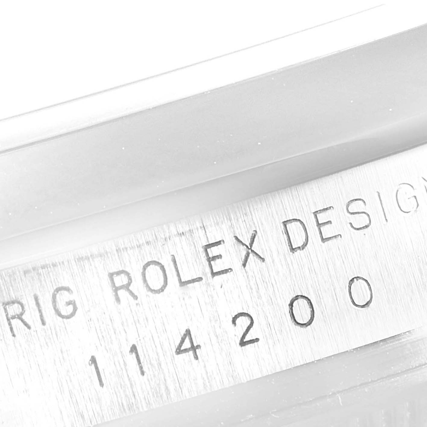 The image shows the side view of the case of a Rolex Oyster Perpetual 114200 Men
s Stainless Steel Black Dial 114200 Men
s Stainless Steel Black Dial watch, highlighting its engraved serial number.