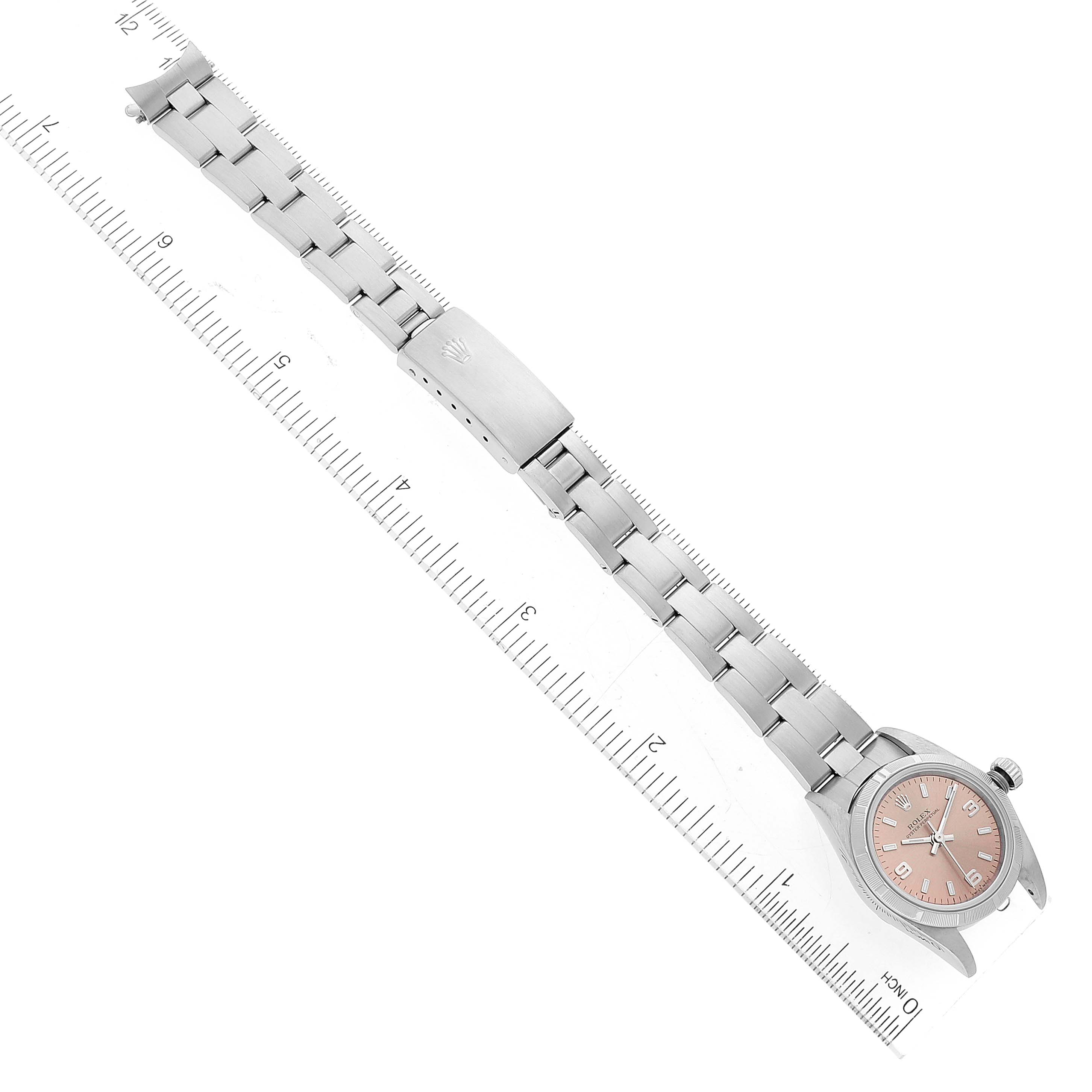 The image shows an overhead view of the Rolex Oyster Perpetual 76030 Women
s Stainless Steel Pink Dial 76030 Women
s Stainless Steel Pink Dial watch, with its metal bracelet and clasp aligned with a ruler.