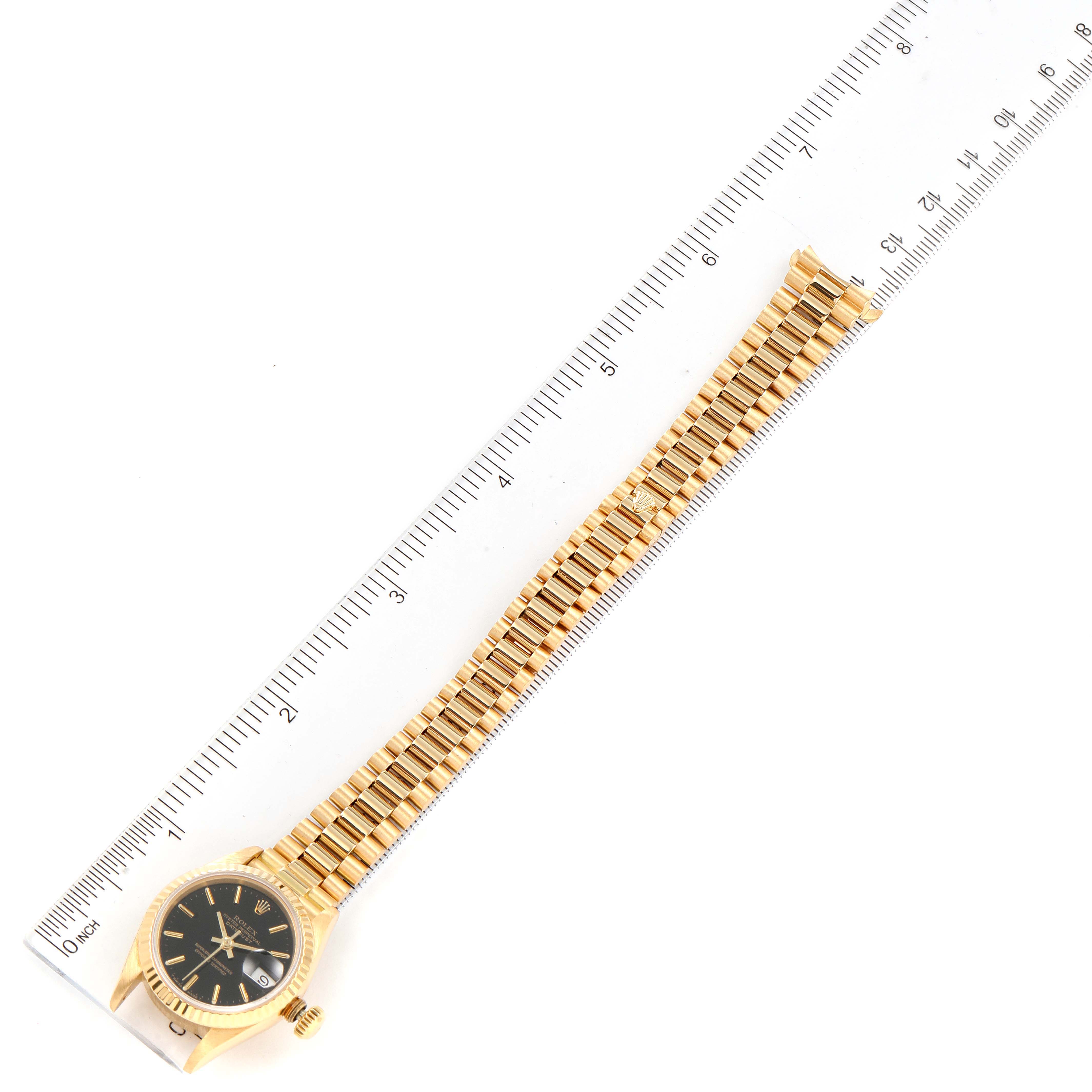 This image shows a top-down view of a Rolex President 69178 Women's Yellow Gold Black Dial 69178 Women's Yellow Gold Black Dial model watch with its bracelet next to a ruler for measurement.