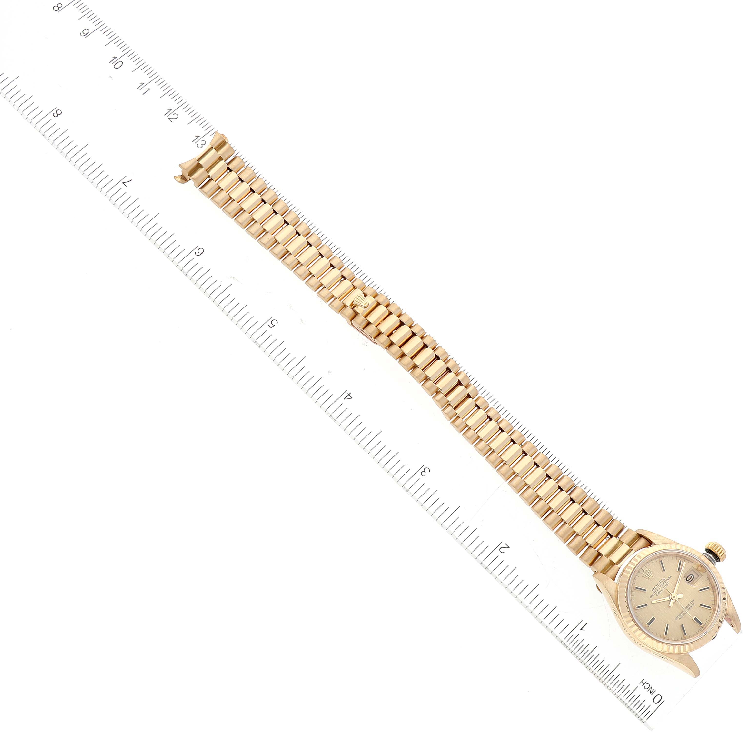 The image shows a top view of a Rolex President 69178 Women
s Yellow Gold Champagne Dial 69178 Women
s Yellow Gold Champagne Dial model watch, aligned with a ruler for size reference, focusing on its face, crown, and full band.