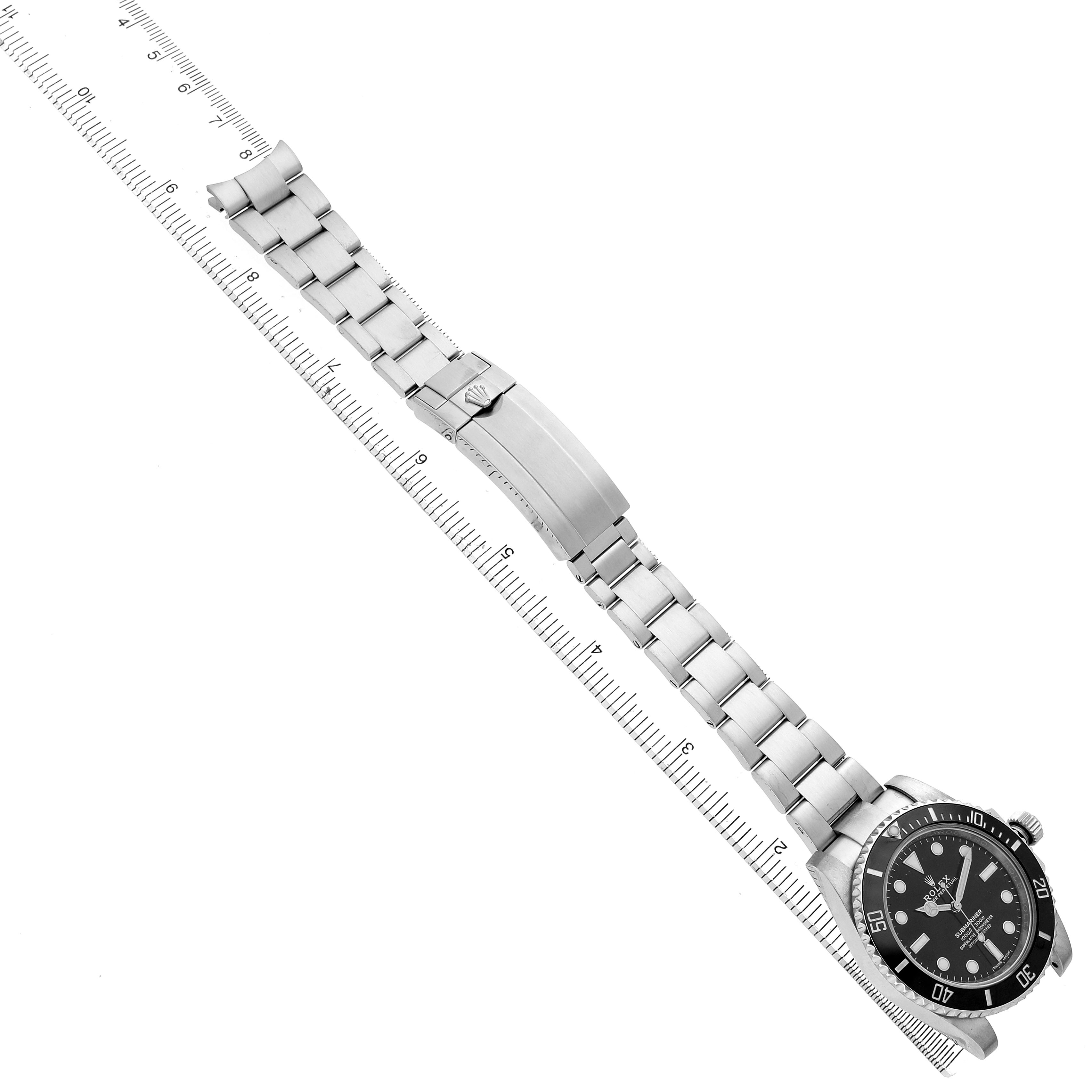 The Rolex Submariner 114060 Men's Stainless Steel Black Dial watch is shown at an angled top view, displaying the dial, bezel, bracelet, and clasp with a ruler beside it.