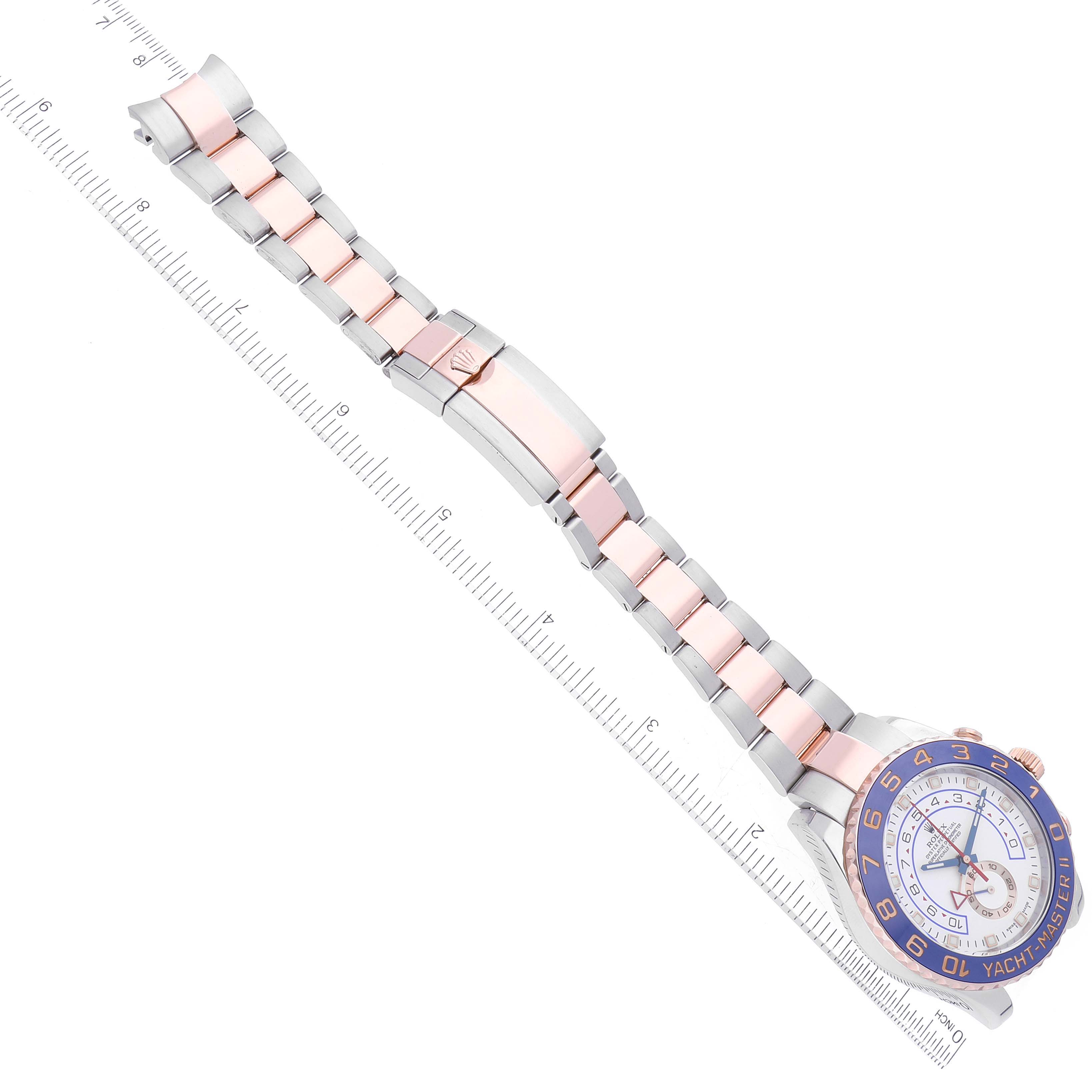 The image shows an overhead view of a Rolex Yacht-Master 116681 Men
s Steel and Gold (two tone) White Dial 116681 Men
s Steel and Gold (two tone) White Dial watch, displaying its face and metal strap alongside a ruler.